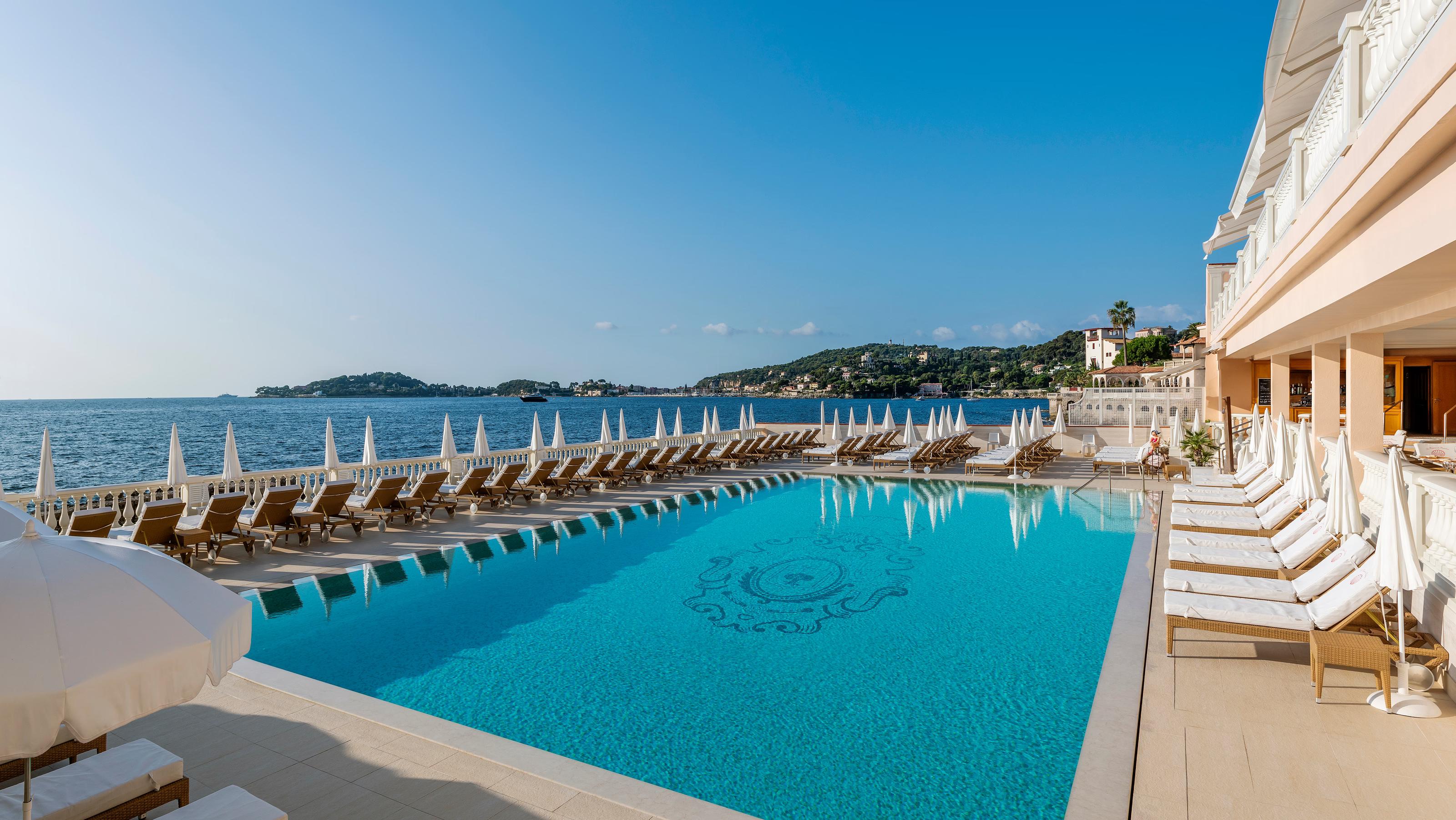 Heated seawater pool lined with white loungers overlooking the Mediterranean