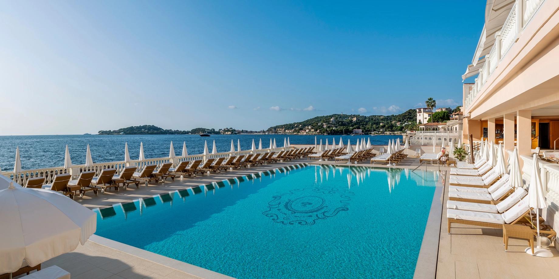 Heated seawater pool lined with white loungers overlooking the Mediterranean