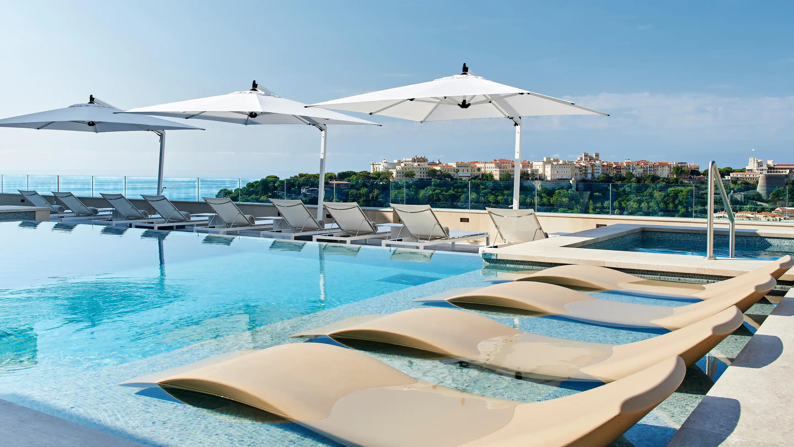 Hôtel de Paris Monte-Carlo: rooftop pool with blue water, white umbrellas, and lounge chairs overlooking water