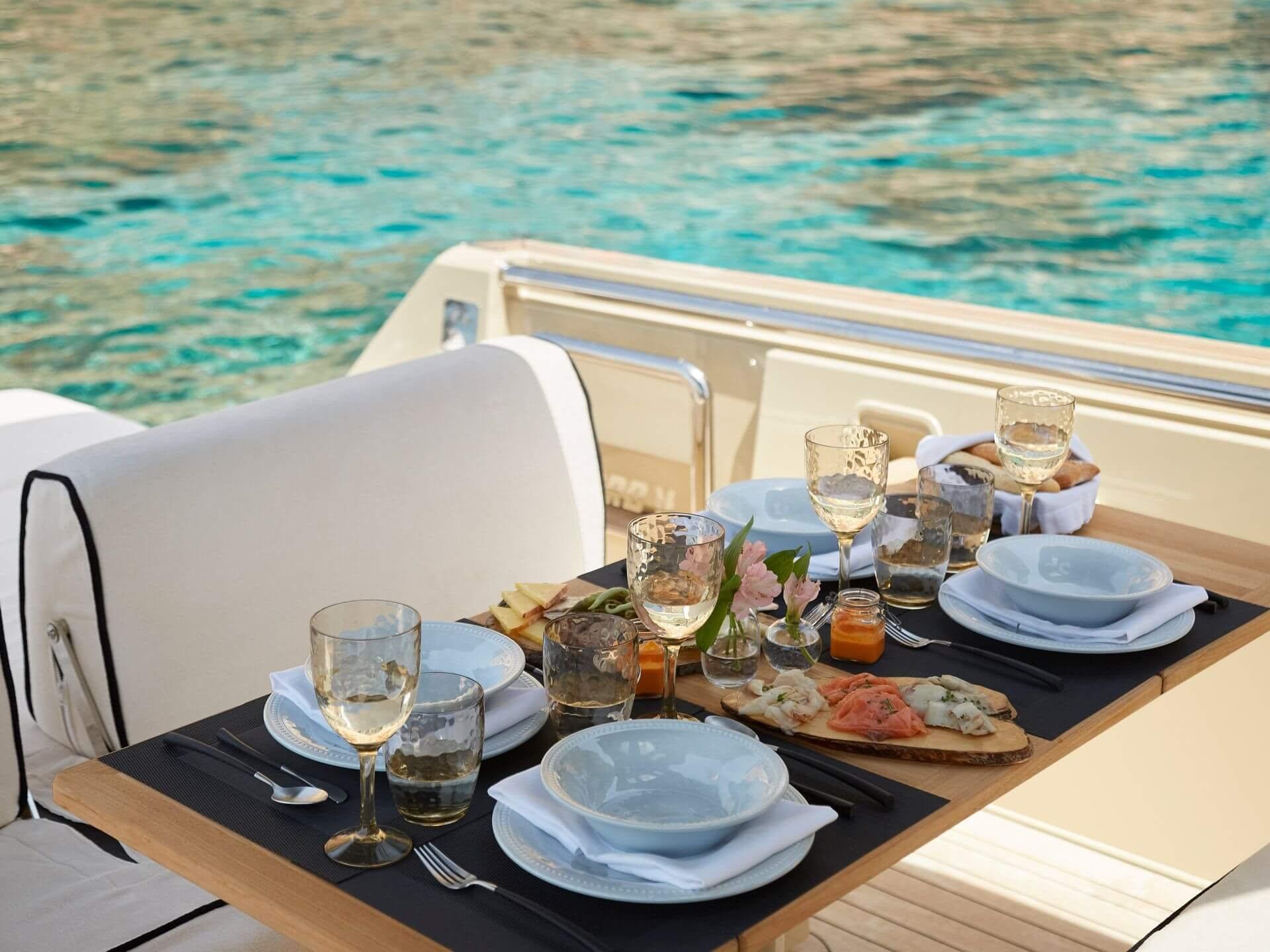Cap Rocat: a table setting on a boat overlooking turquoise waters, wine glasses, and blue dishware