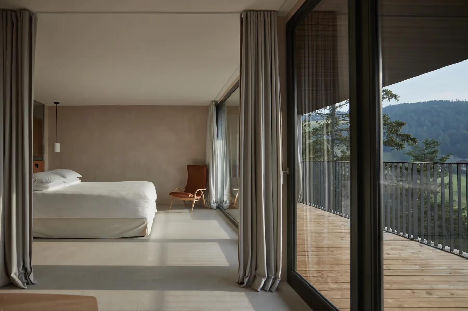 Bright bedroom with white bedding, wood accents, and open doors to a terrace with mountain views