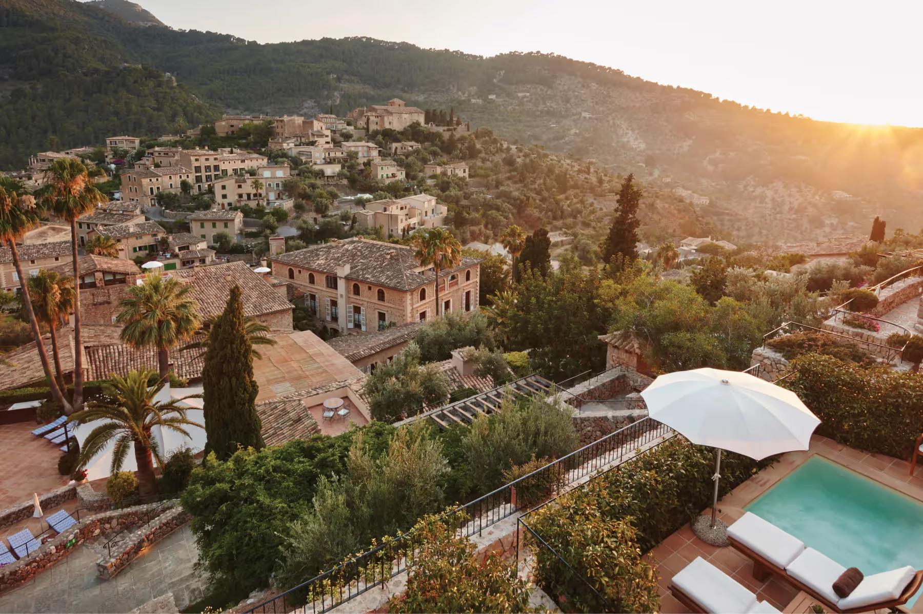 La Residencia: resort buildings at sunset overlooking hillside with pool, cypress trees, and Mediterranean view