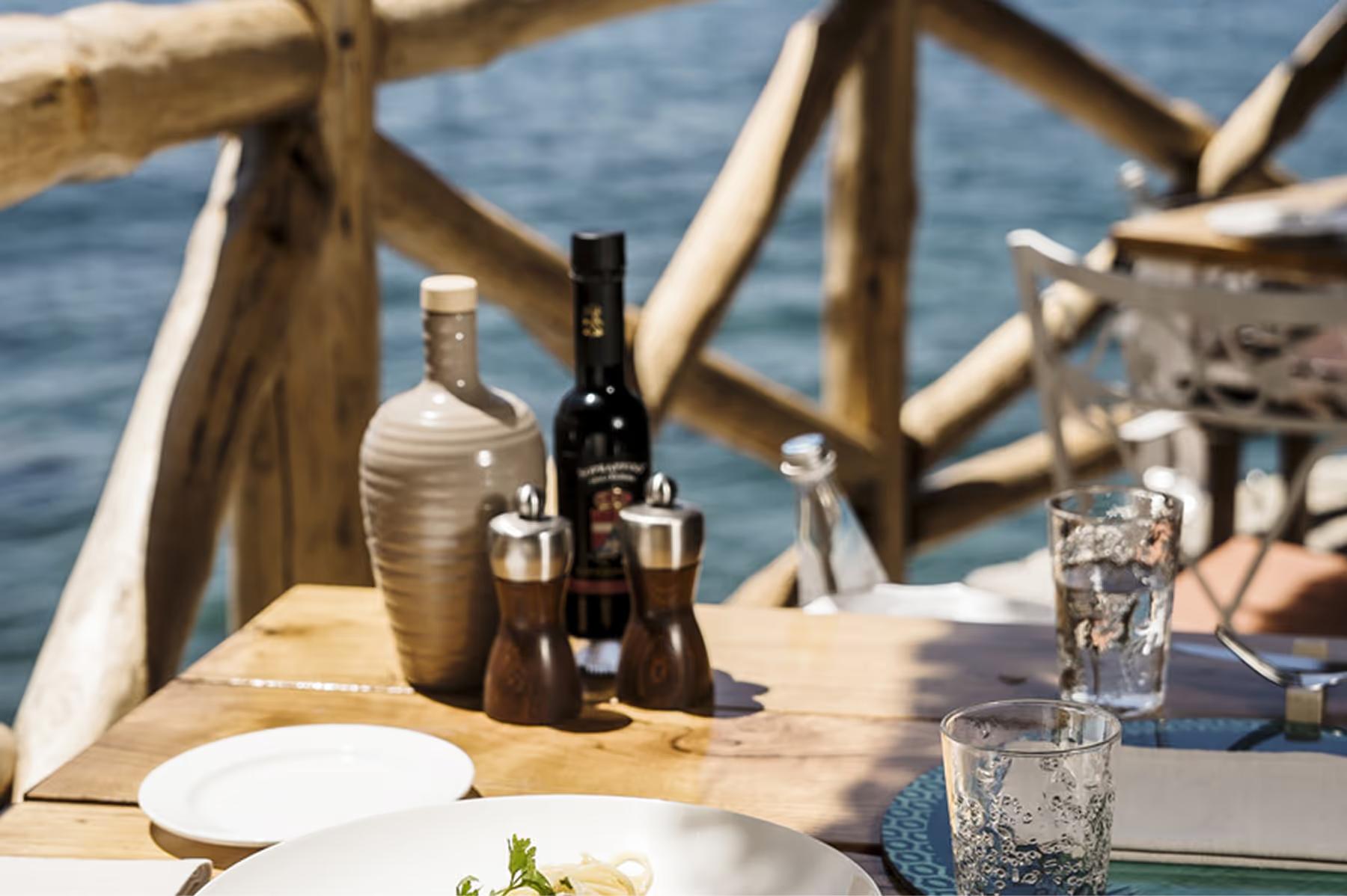Il San Pietro di Positano: place setting on wooden table with wine bottles, glasses, and driftwood railing overlooking sea