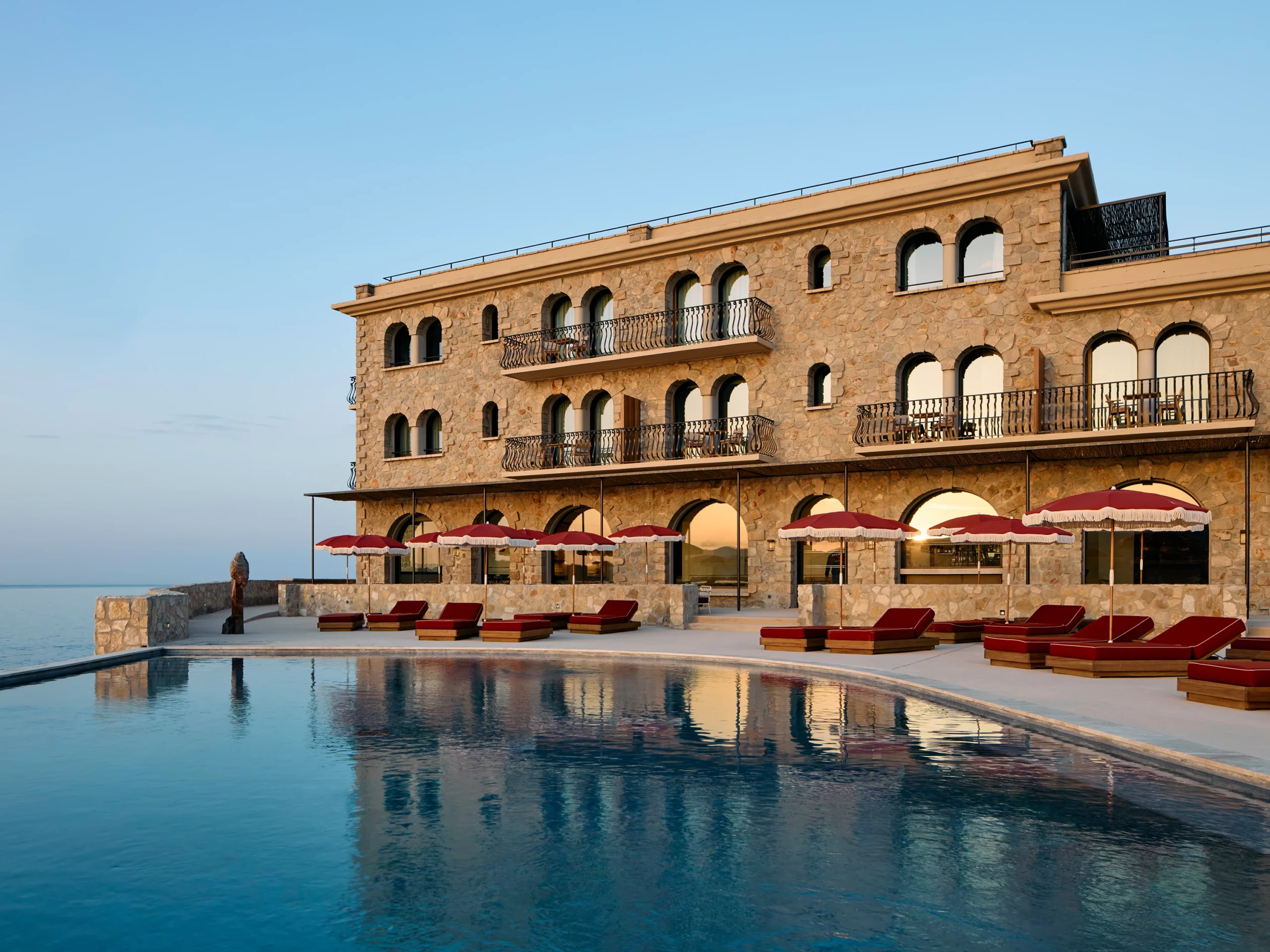 Zannier Île de Bendor: fringed red parasols and loungers line the pool as the stone hotel glows at dusk