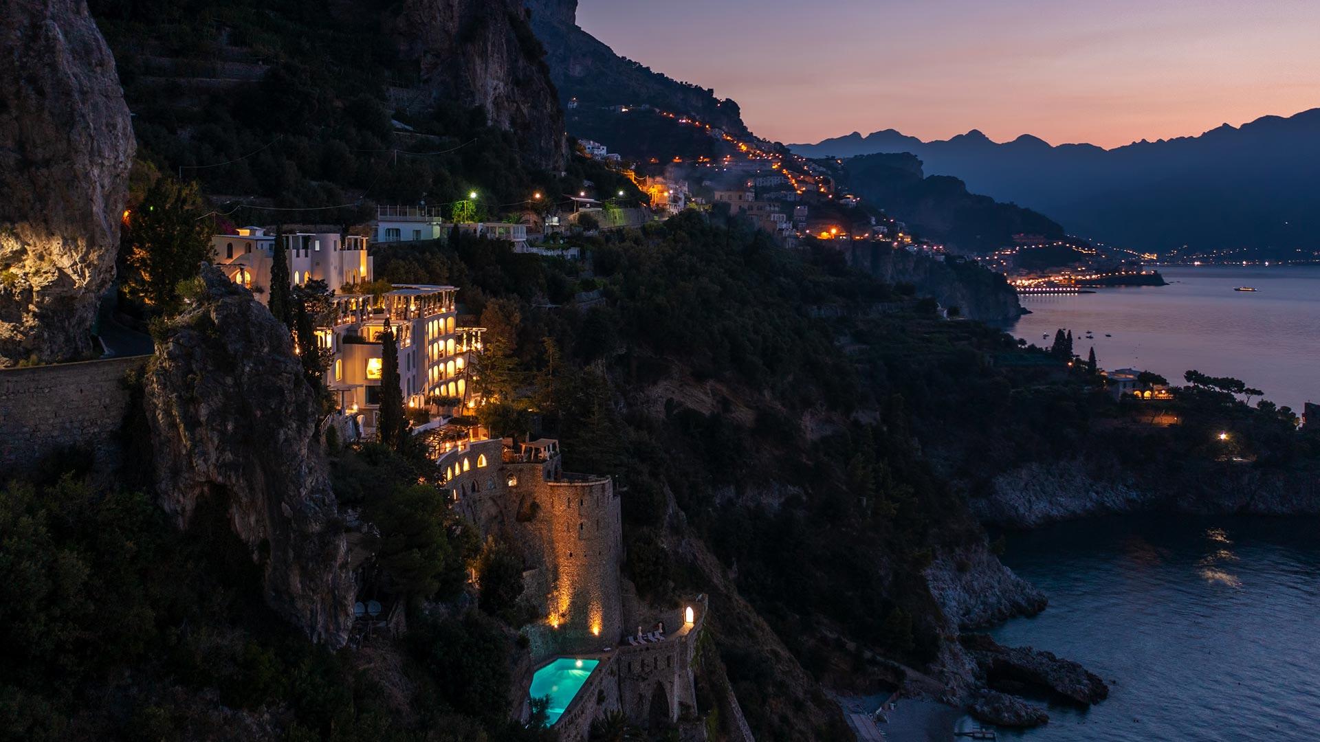 Borgo Santandrea: cliffside property lit at twilight with illuminated terraces cascading down the slope