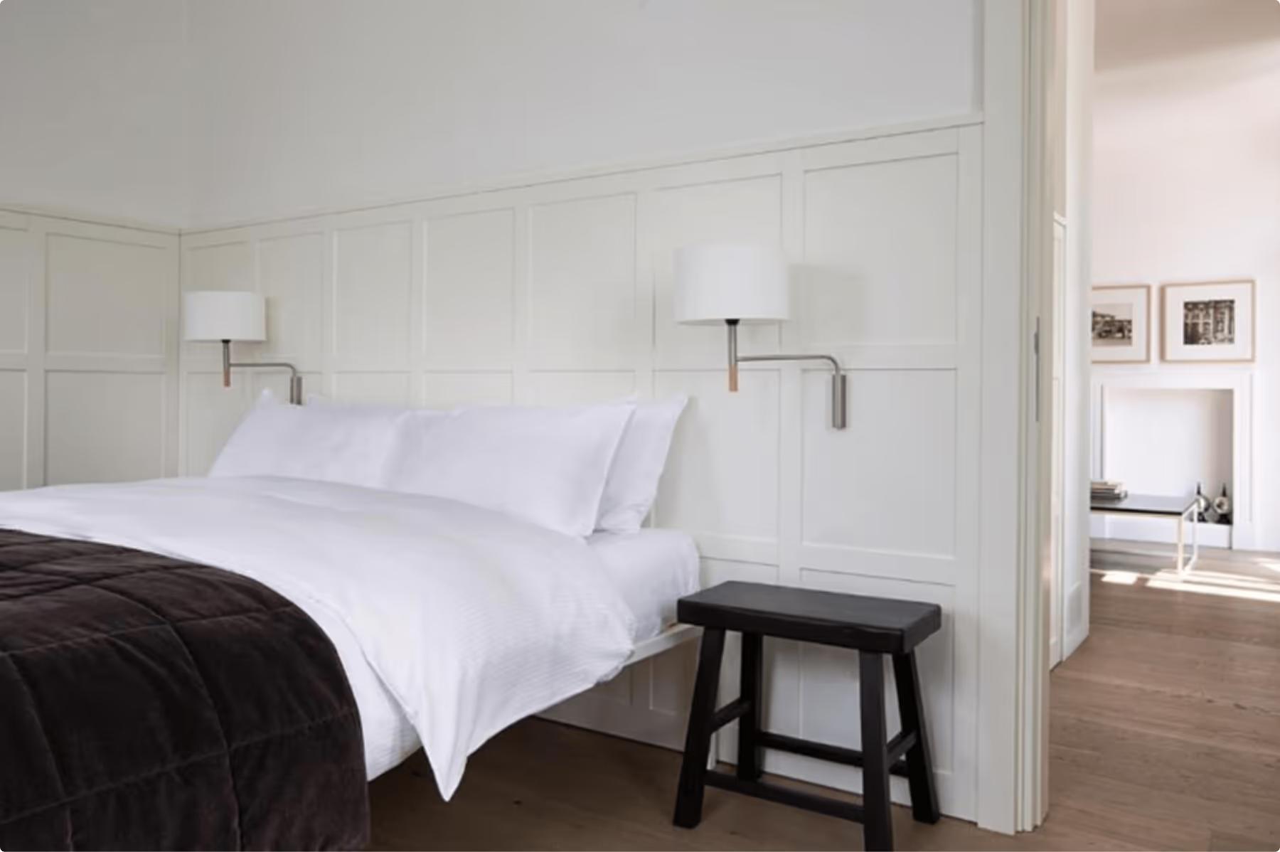 Minimalist bedroom with white linens and tall arched windows framing lake views