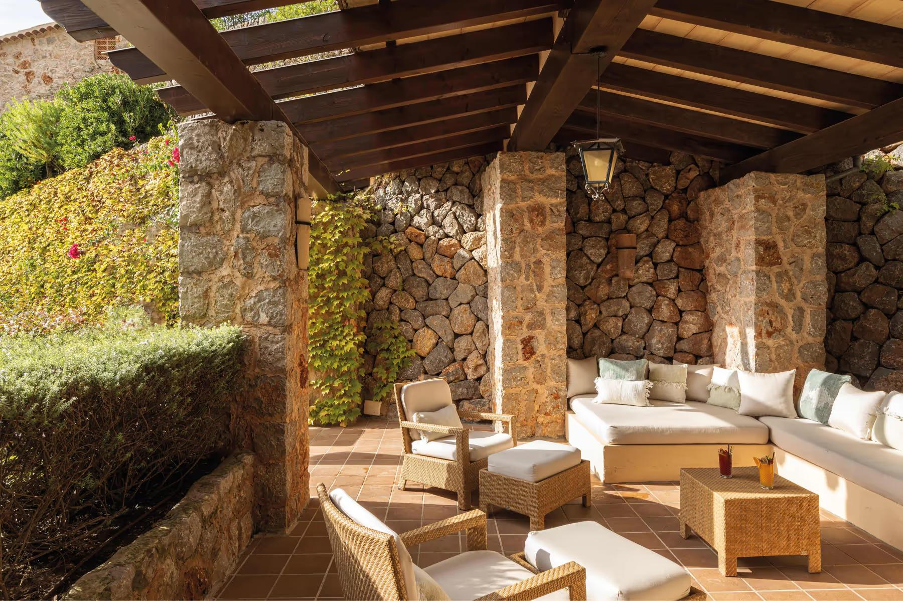 Covered patio with stone walls, wooden pergola, and cream-colored lounge seating