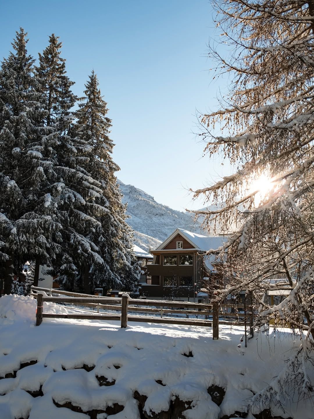 A snow-covered chalet in Andermatt with the sun breaking through frosted trees