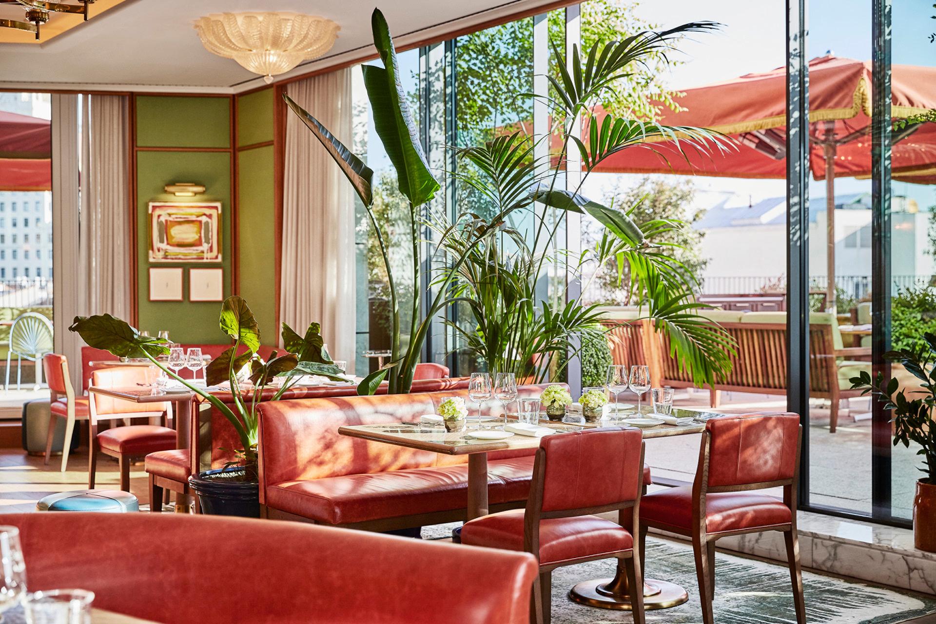 Four Seasons Hotel Madrid: rooftop dining terrace with coral seating, tropical plants, and skyline views through glass doors