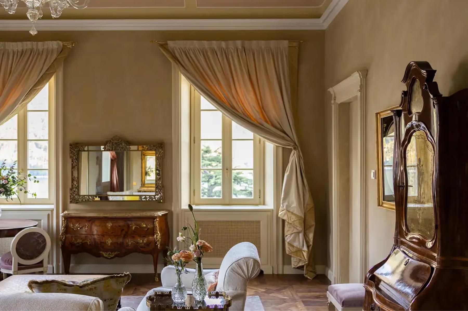 A bedroom with cream walls, ornate desk, and fabric draping from gilded cornice