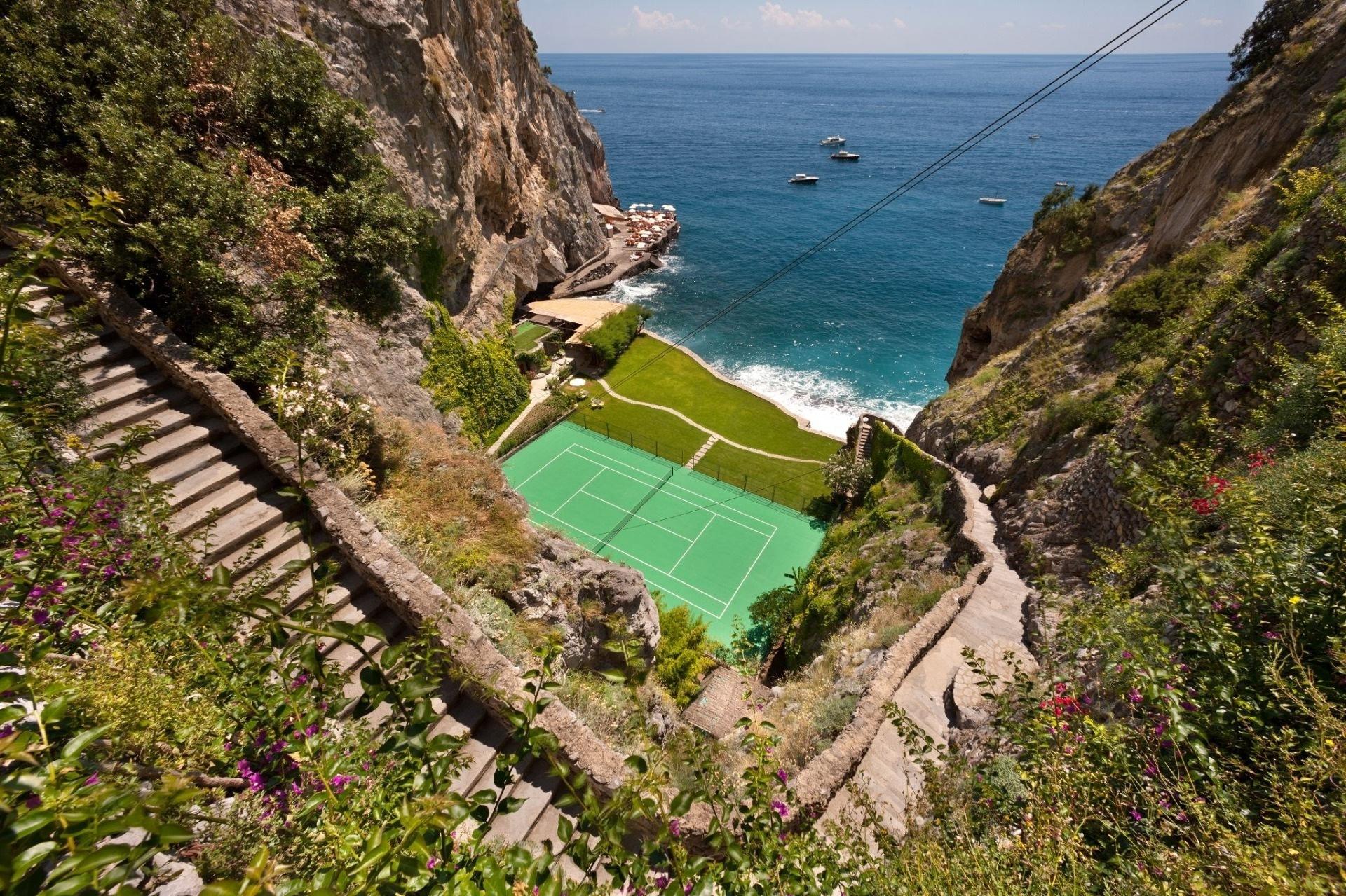 Il San Pietro di Positano: green tennis court carved into cliffside between green vegetation and bright Mediterranean sea