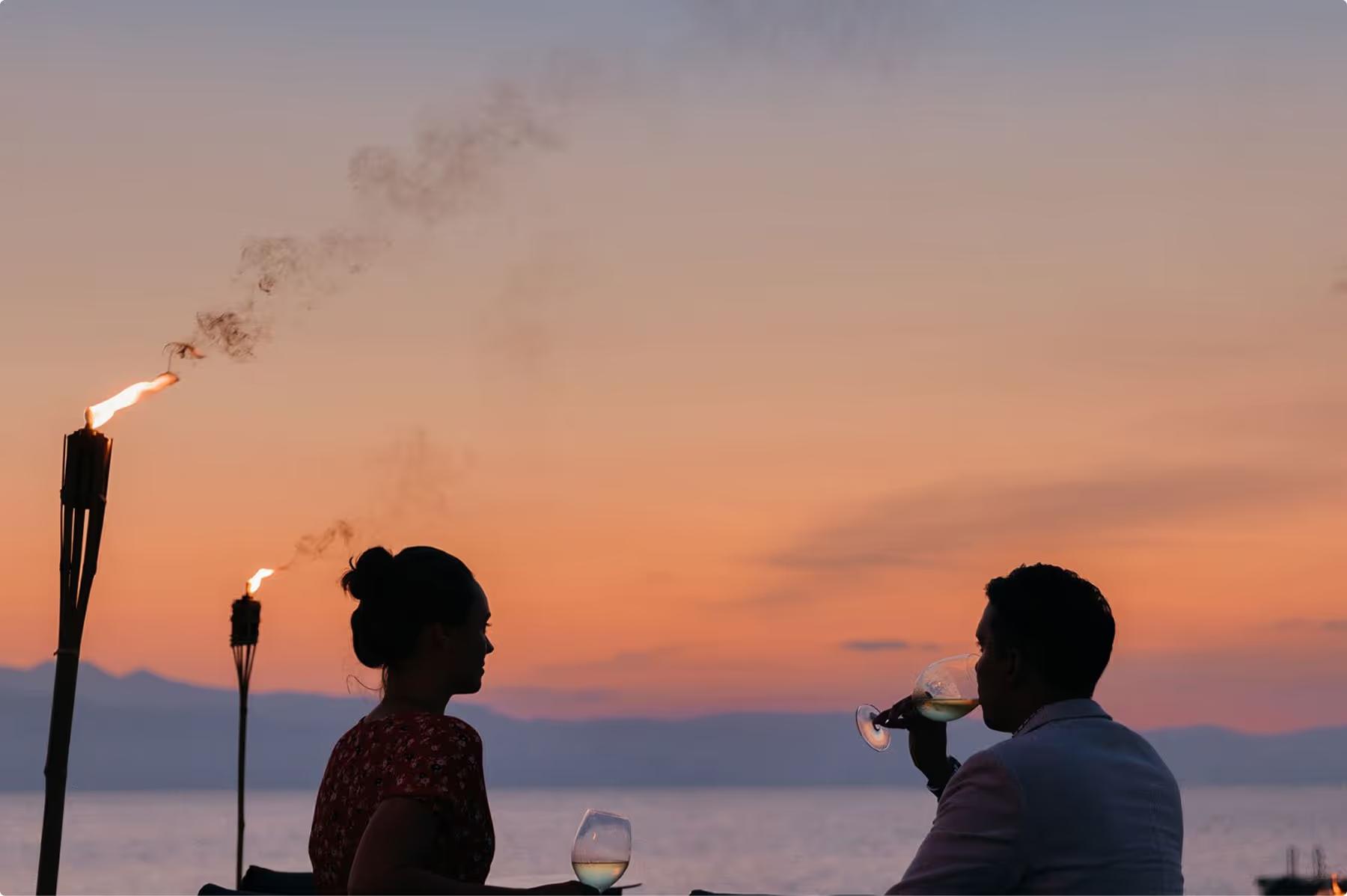 Couple dining at sunset with torch lighting and bay views