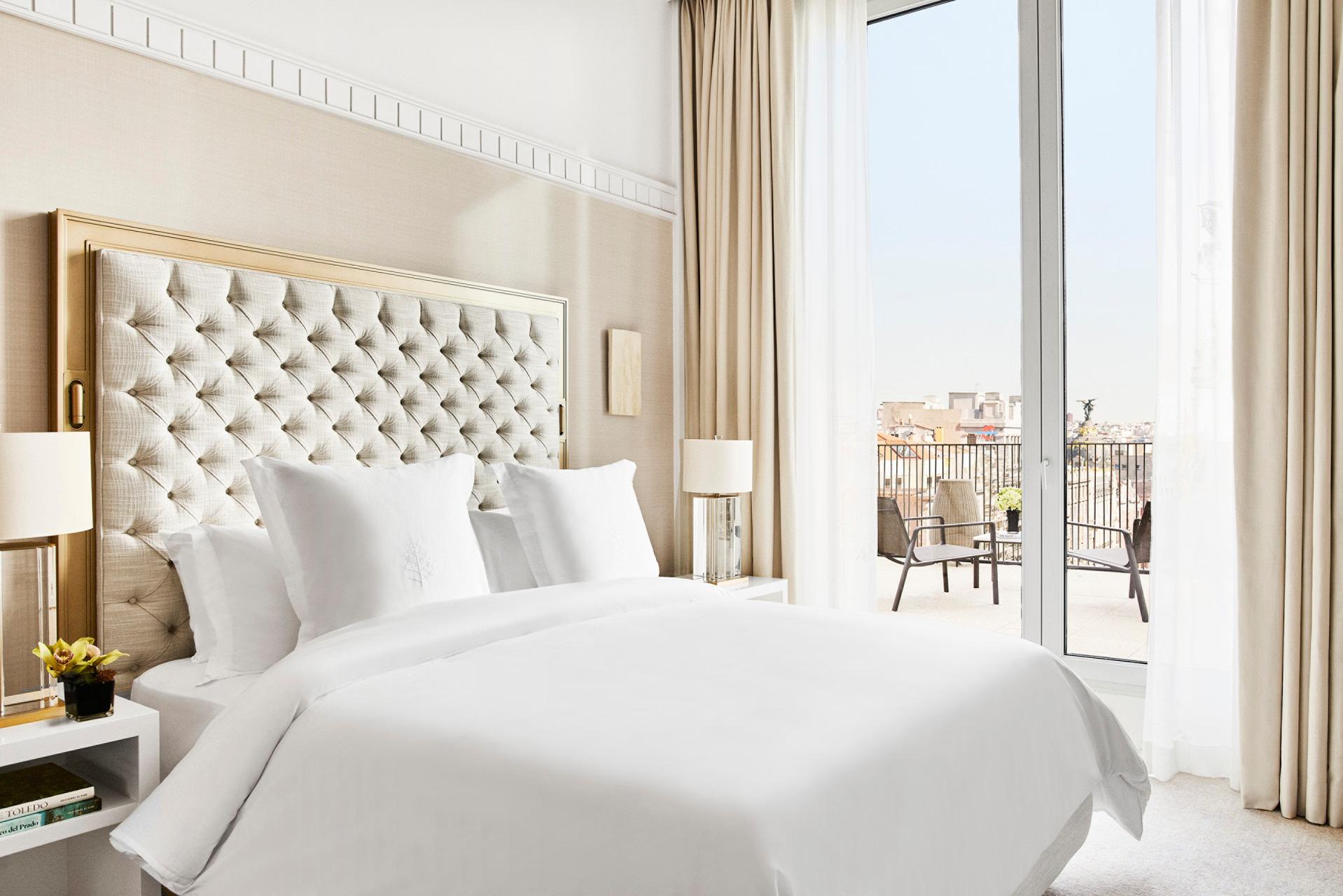 Bedroom with white quilted headboard, floor-to-ceiling windows, and balcony overlooking Madrid skyline