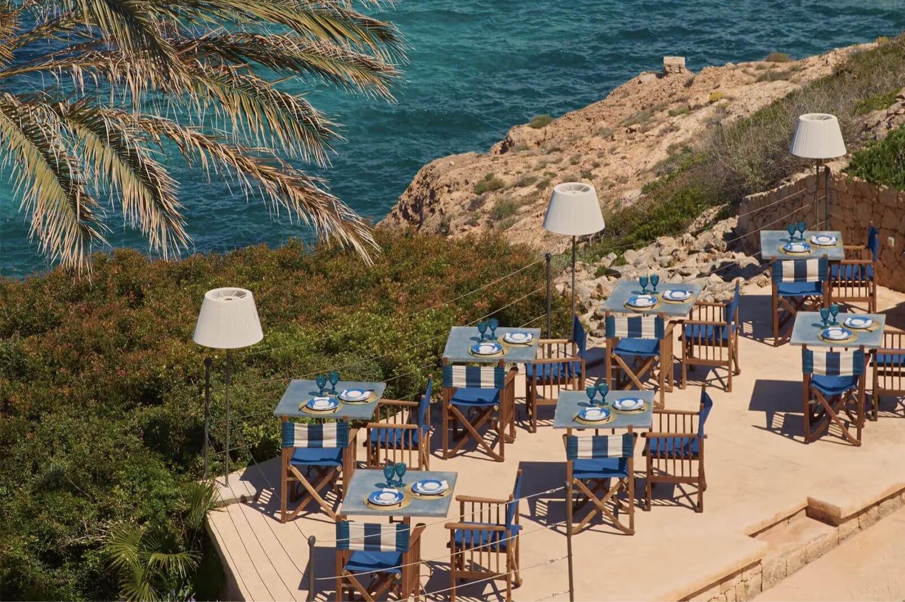 Cap Rocat: a beachside dining setup with wooden tables, purple accents, and panoramic seascapes