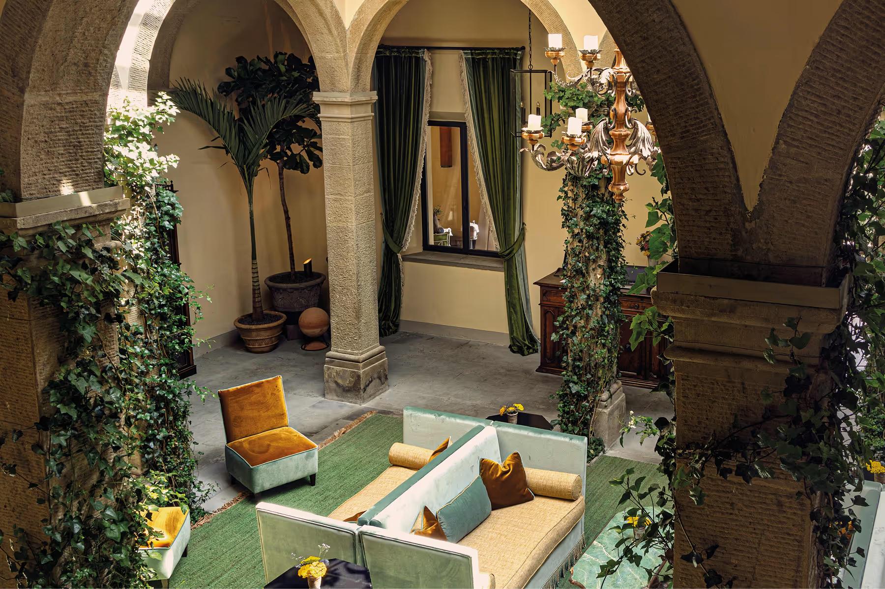 Villa San Michele: monastic courtyard with barrel vaults, cream seating, green drapes, climbing ivy, and ornate gilt chandelier