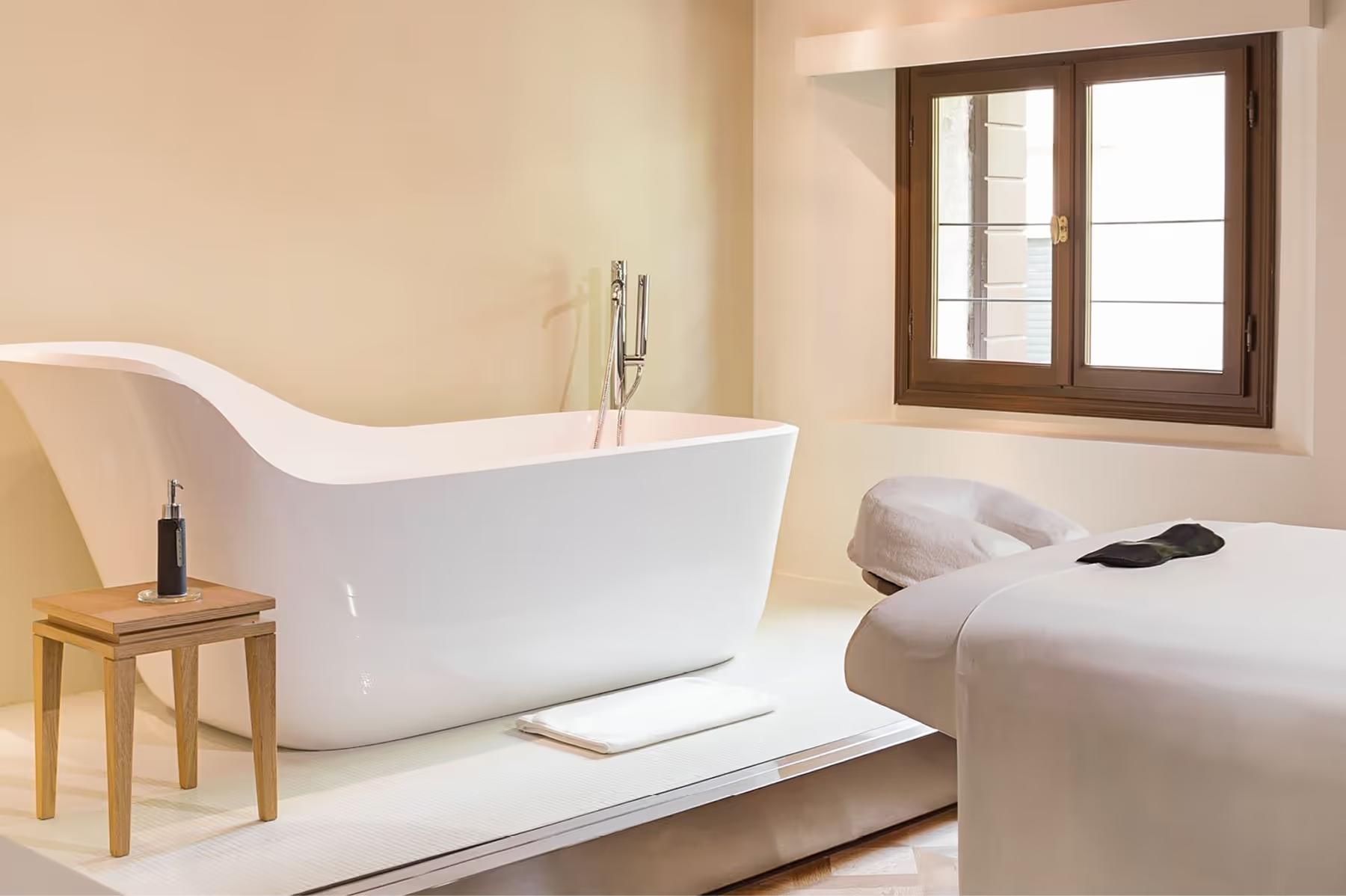 Aman Venice: a spa bathroom with a freestanding white stone tub, stepped platform, and window with natural light