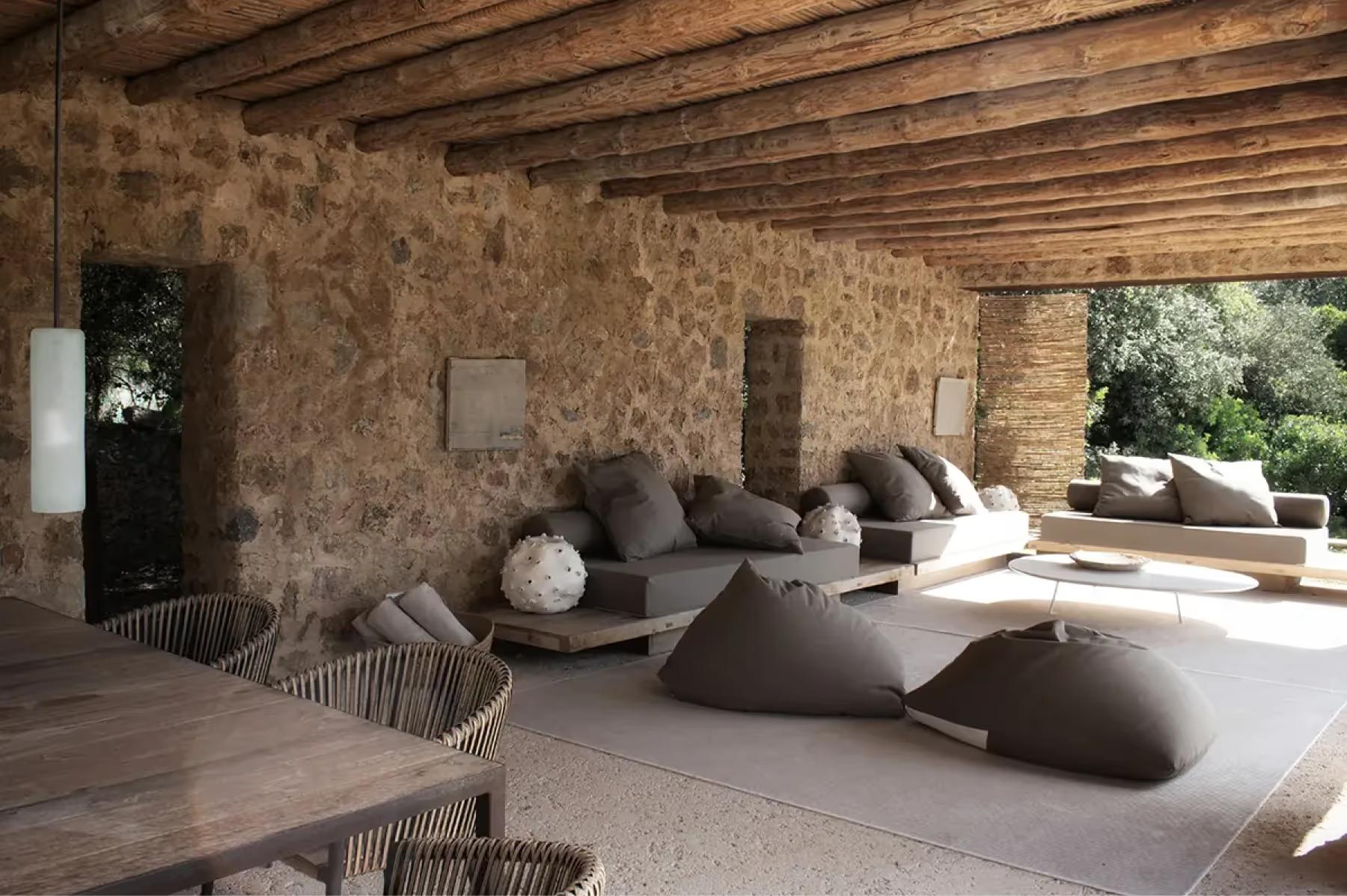 Es Racó d’Artà: covered outdoor lounge with curved concrete seating, timber framework, and natural stone walls