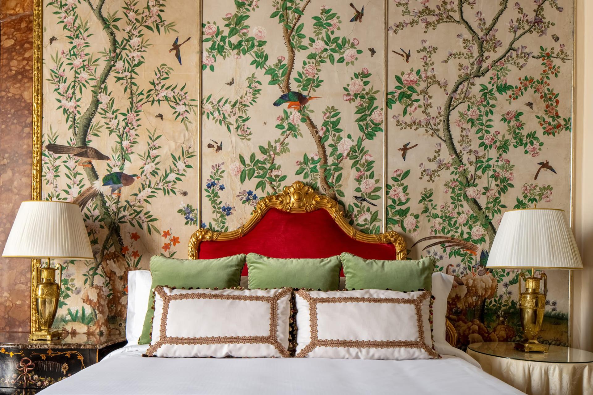 Bedroom with pale headboard upholstered in green, botanical mural behind bed, and brass bedside lights