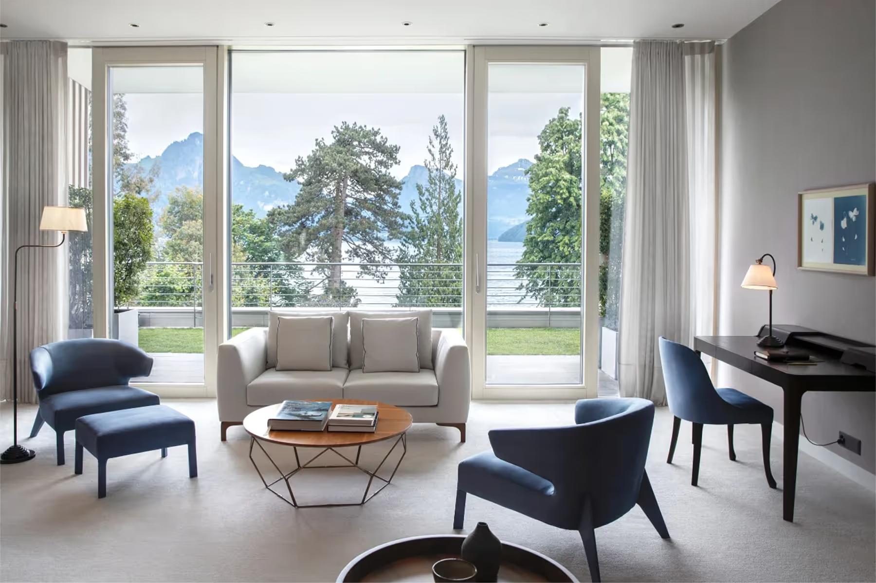 Modern sitting area with large windows, gray sofa, wood accent table, and Alpine views