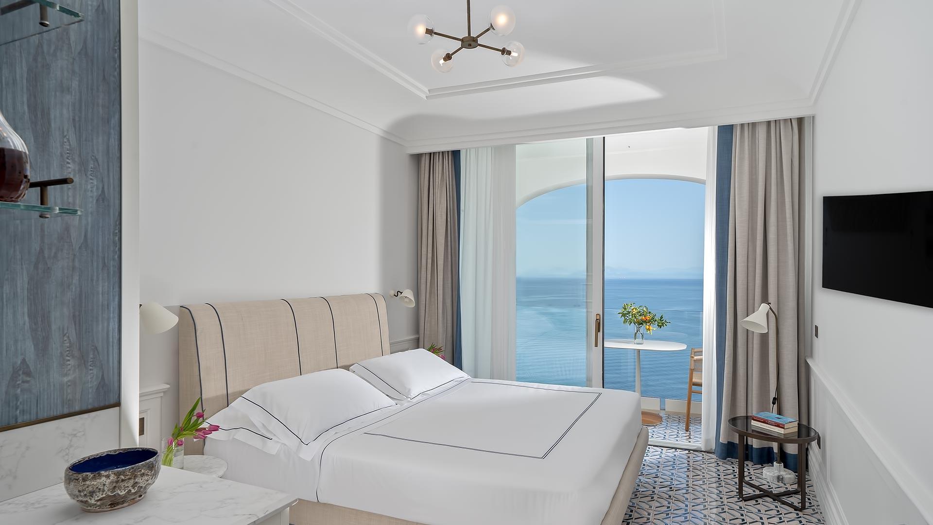 Modern suite with upholstered headboard, ocean-facing balcony, and soft neutral tones