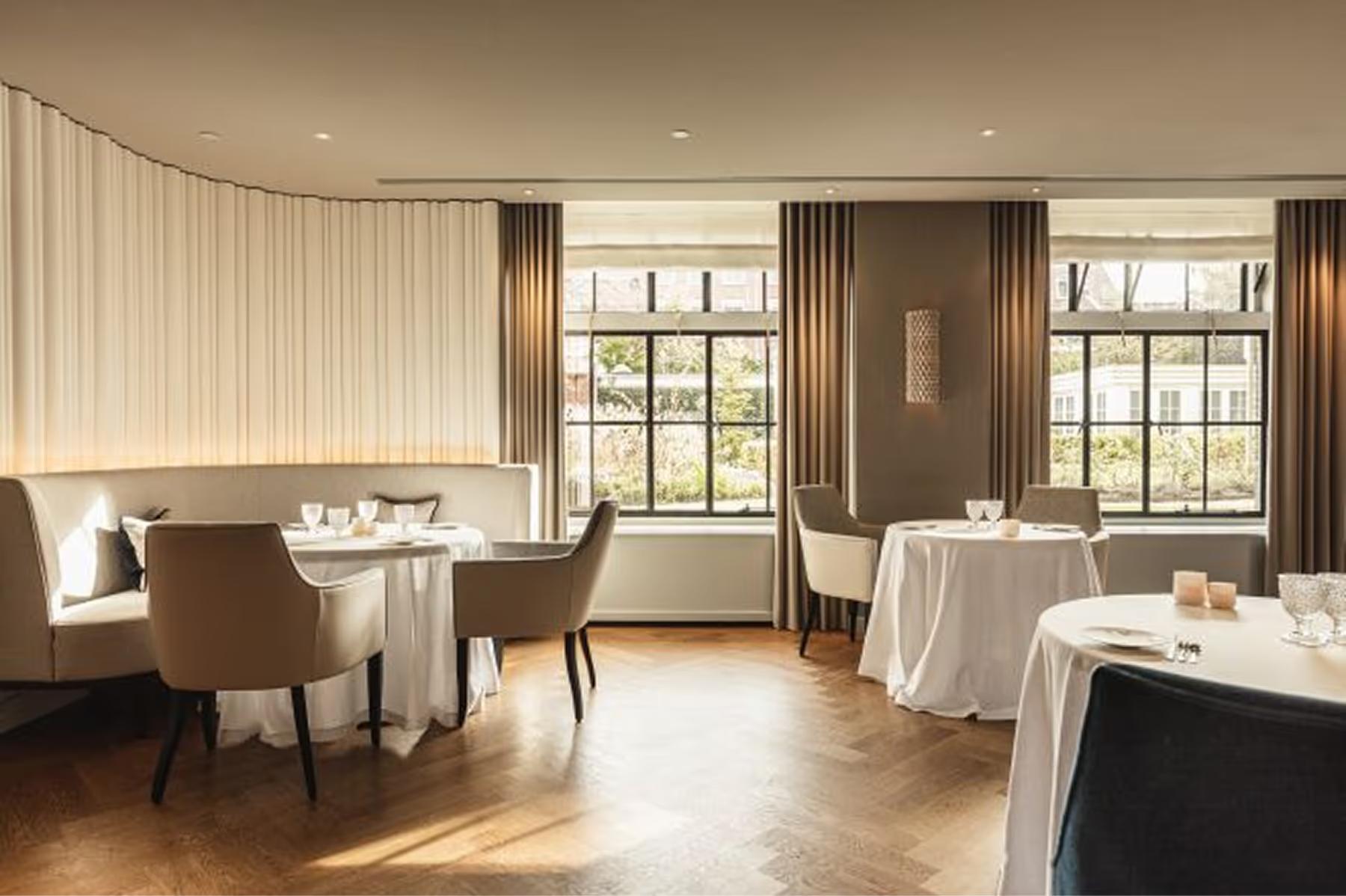 Waldorf Astoria Amsterdam: a formal dining room with cream curtains, natural light from tall windows, and white linens on spaced tables