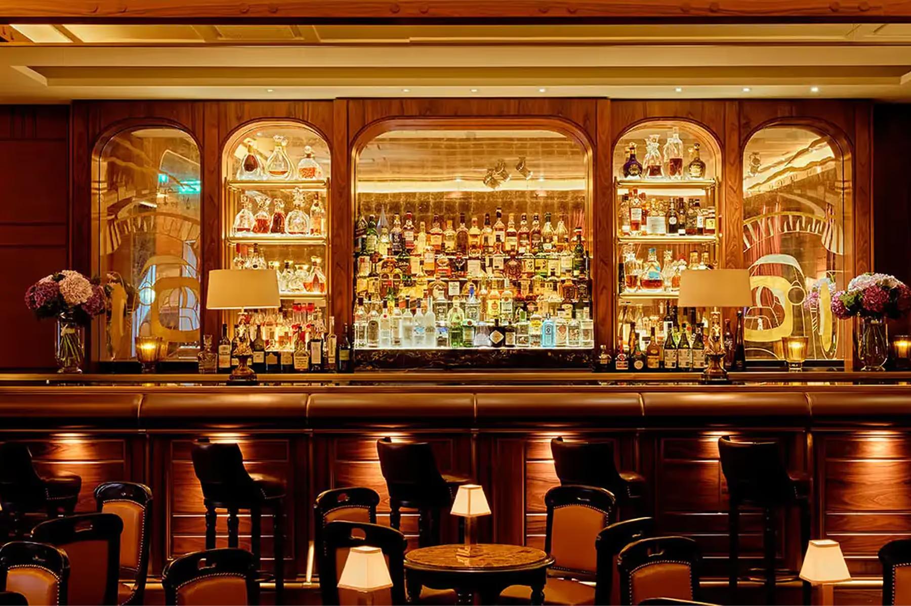 Bar with rich wood paneling, gilt mirrors, and illuminated liquor shelves