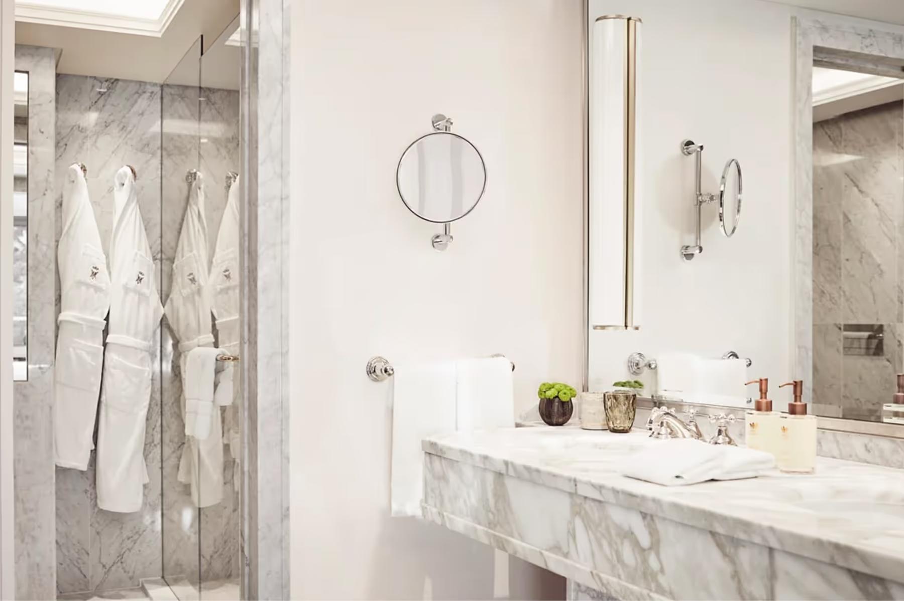 A marble bathroom with dual sinks, mirrored walls, and glass shower enclosure