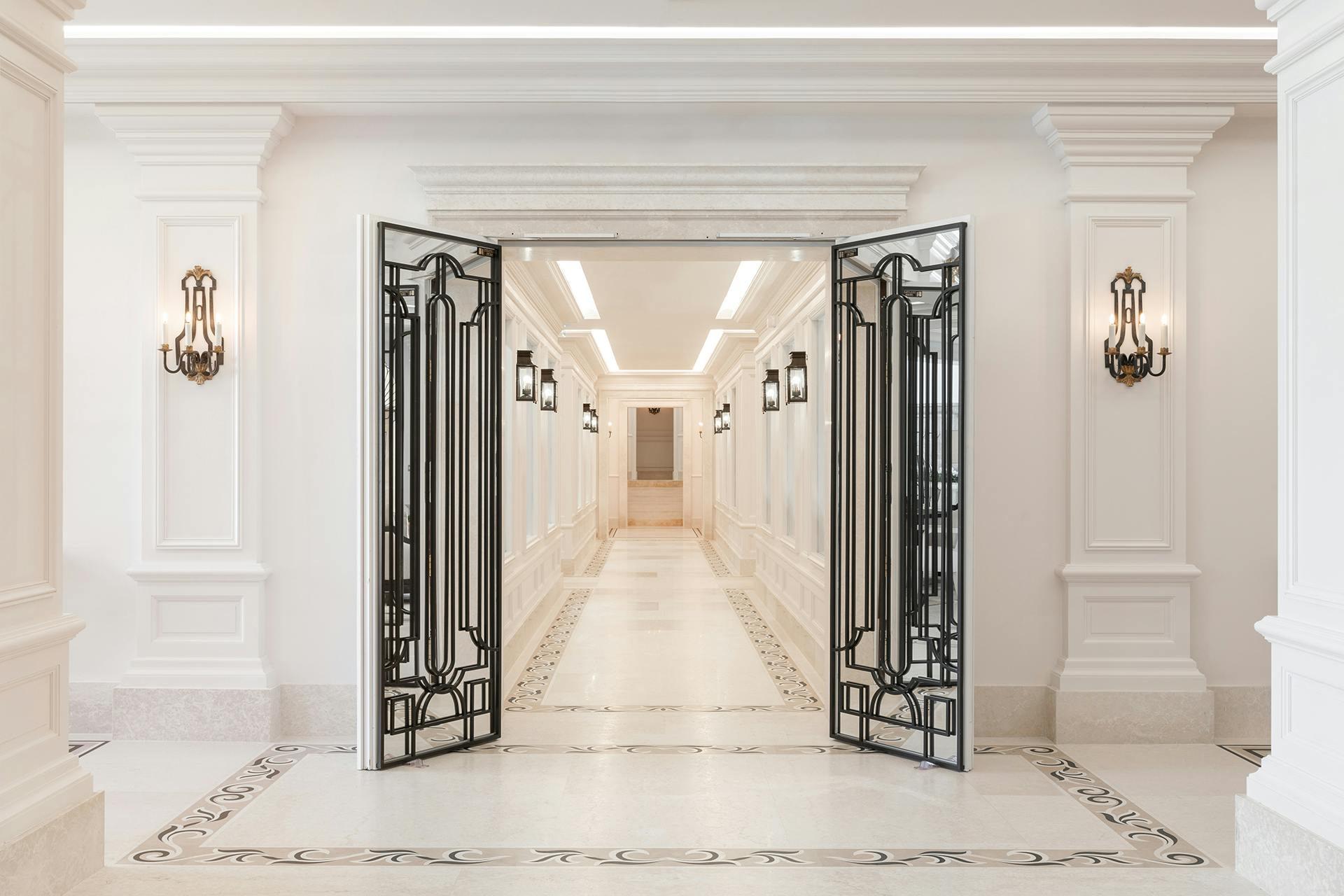 Interior hallway with white stone walls, ornate brass sconces, and decorative iron double doors