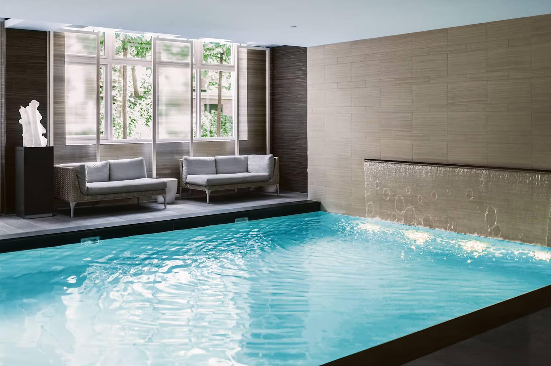 Waldorf Astoria Amsterdam: an indoor pool with rippling turquoise water next to relaxation seating and beige architectural columns
