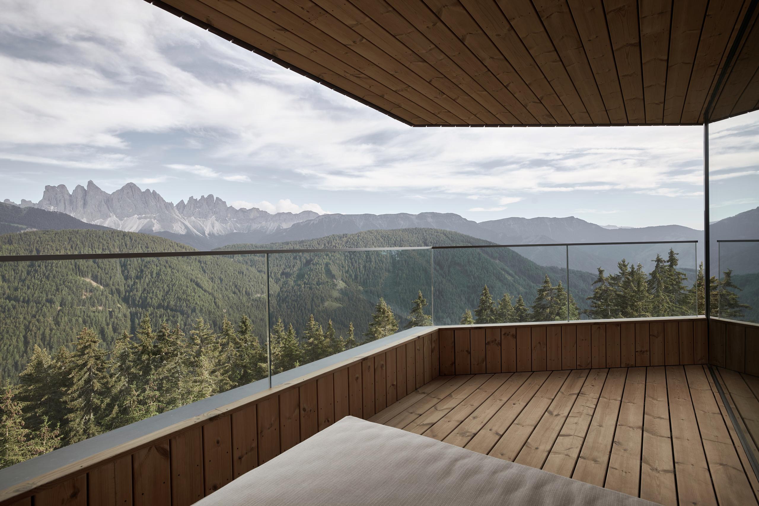 Forestis: a modern guest suite with neutral decor, warm wood floors, and large windows framing landscape views
