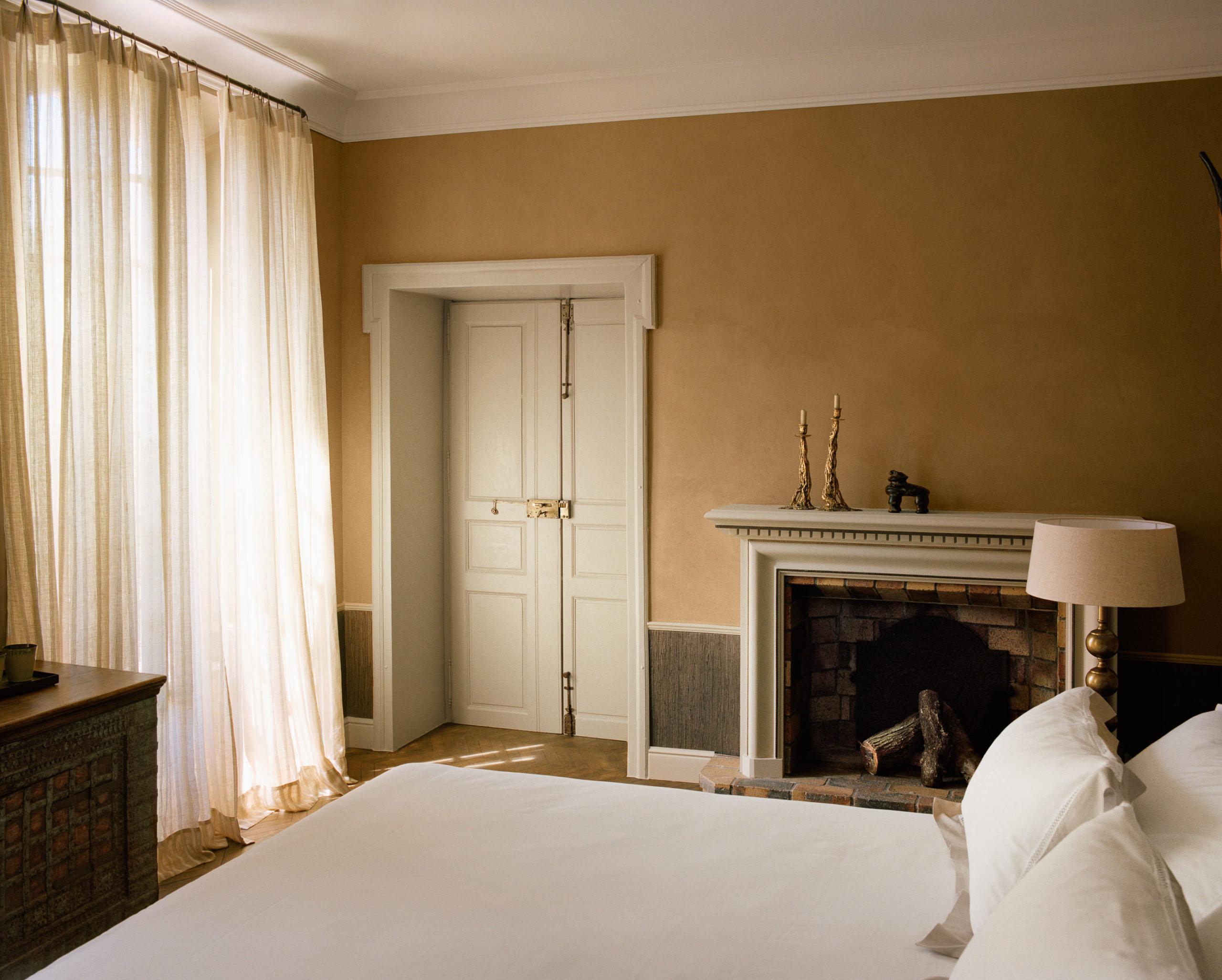Le Mas de Chabran: bedroom with fireplace mantel, multiple windows with flowing curtains, and warm earth tones
