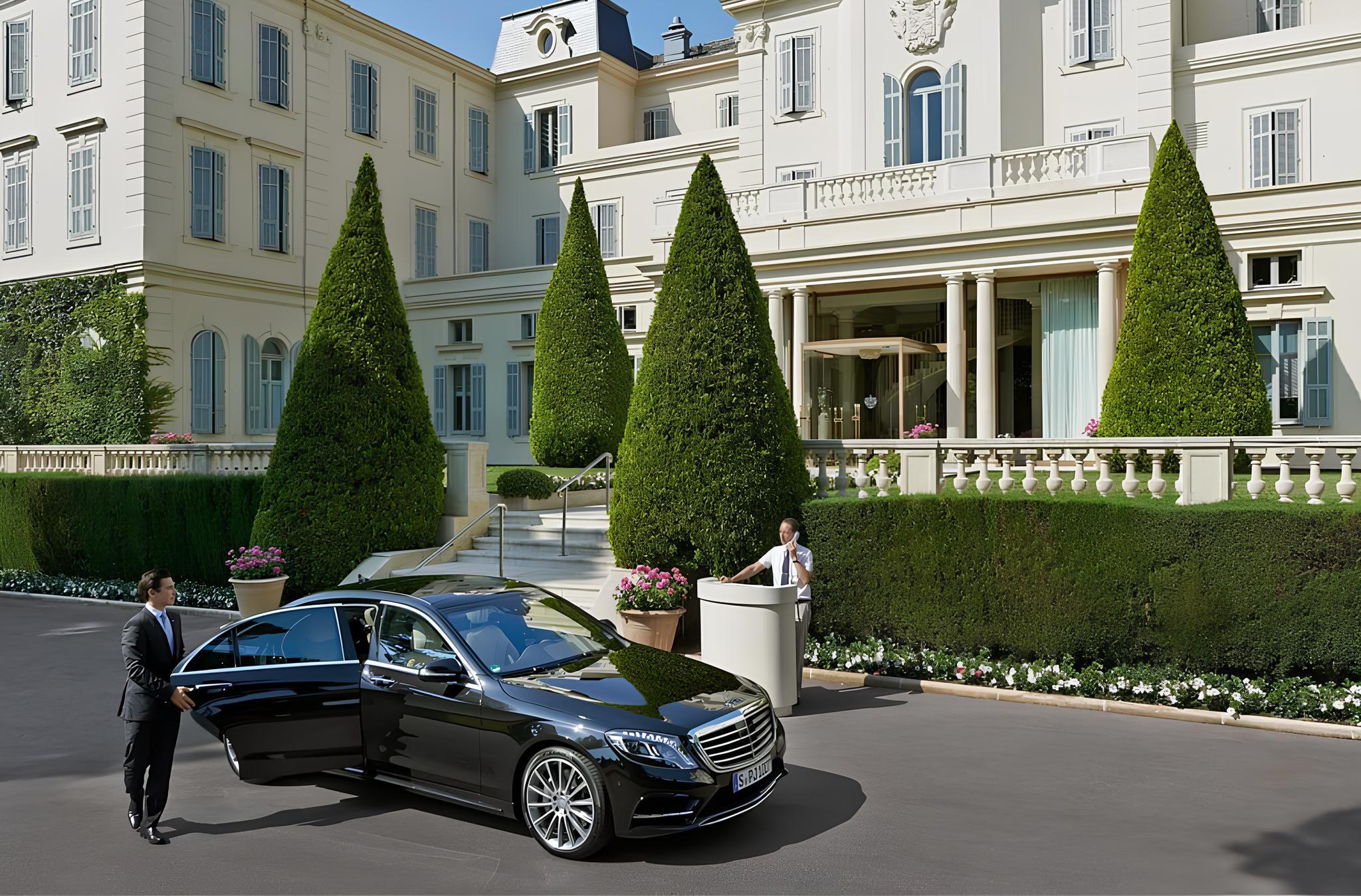 Hotel entrance with a black luxury car and staff, framed by ivy-covered walls and elegant columned portico