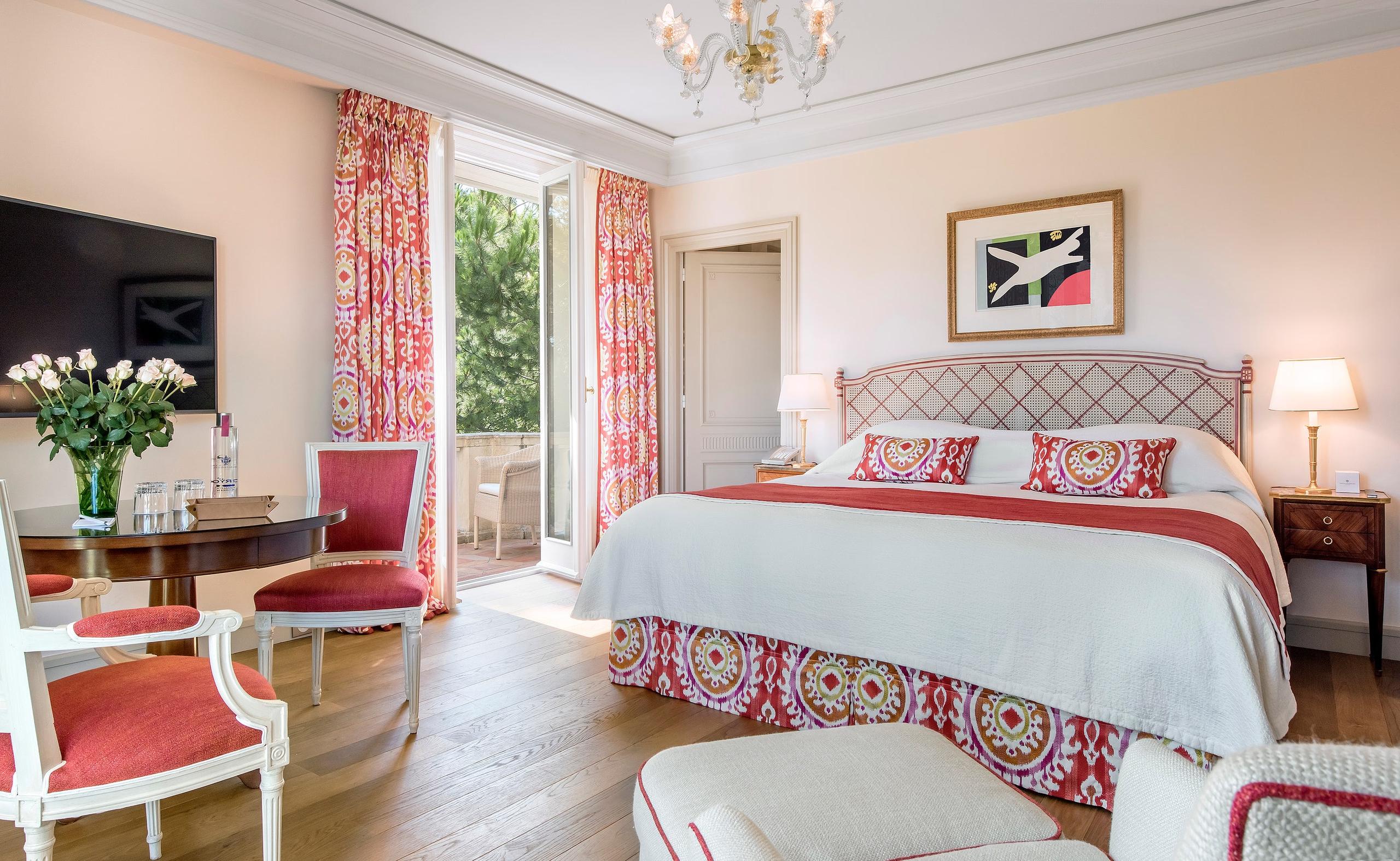 Hôtel du Cap-Eden-Roc: a bedroom with coral and white décor, matching bed covers, patterned curtains, and fresh flowers