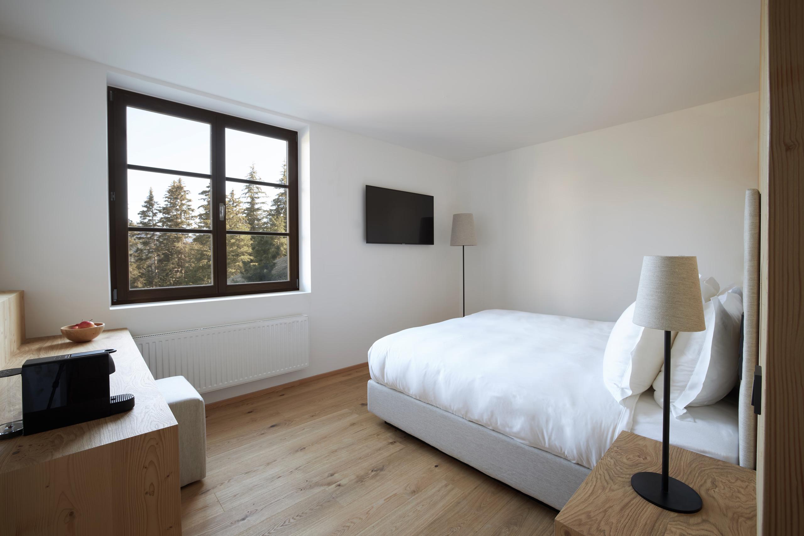 A bright room with a single bed, natural light from a window, and minimal wood and stone furnishings