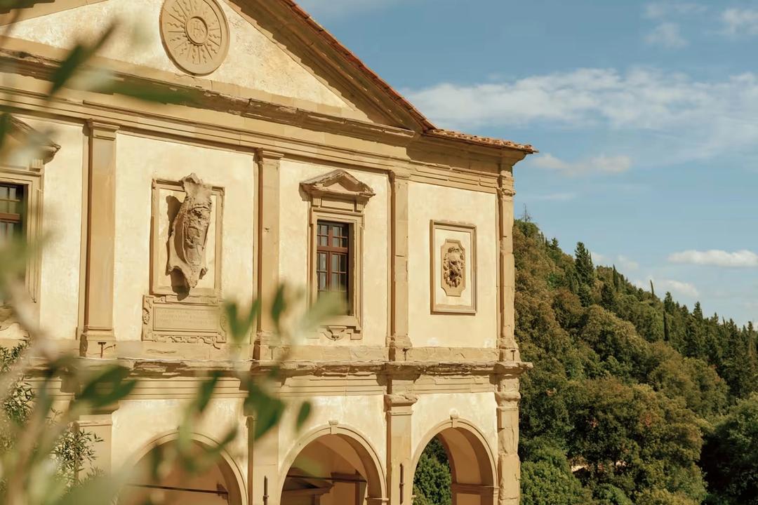 The arcaded facade of Villa San Michele seen through olive branches, with wooded hillside behind