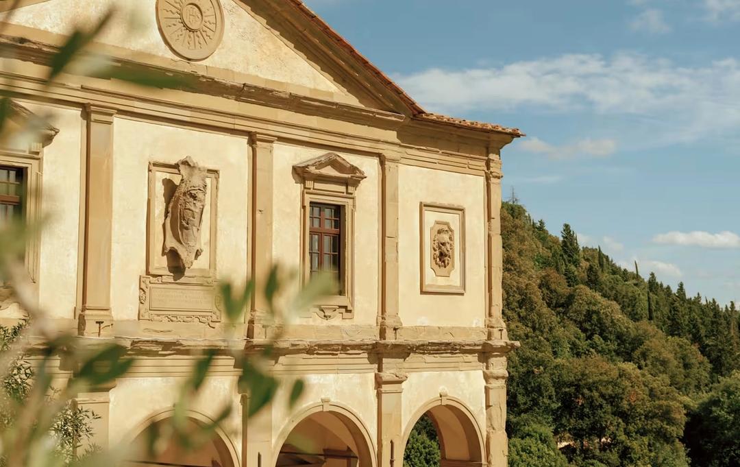 The arcaded facade of Villa San Michele seen through olive branches, with wooded hillside behind