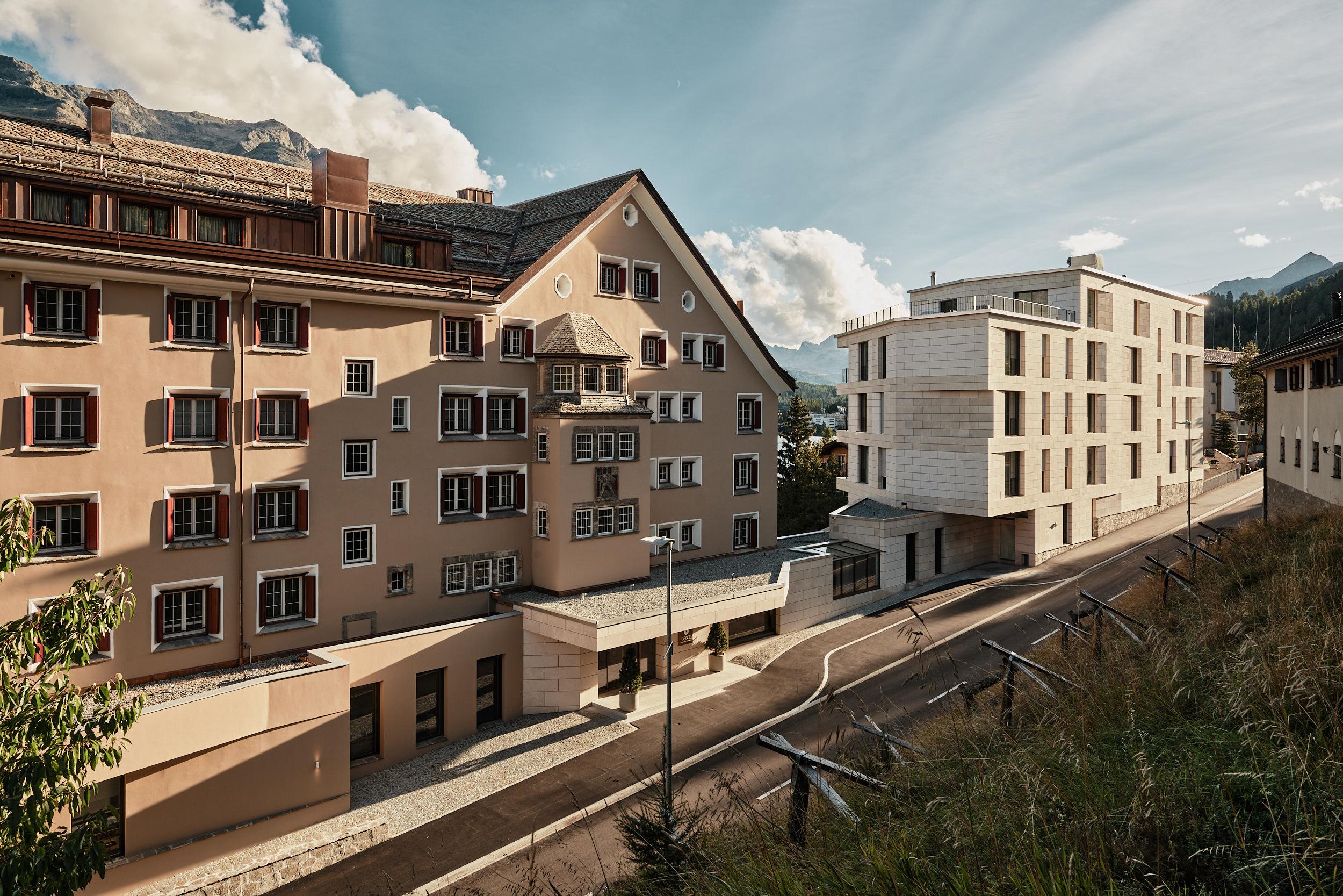 Grace La Margna St. Moritz: historic stone buildings with modern glass addition and mountain backdrop in afternoon sun