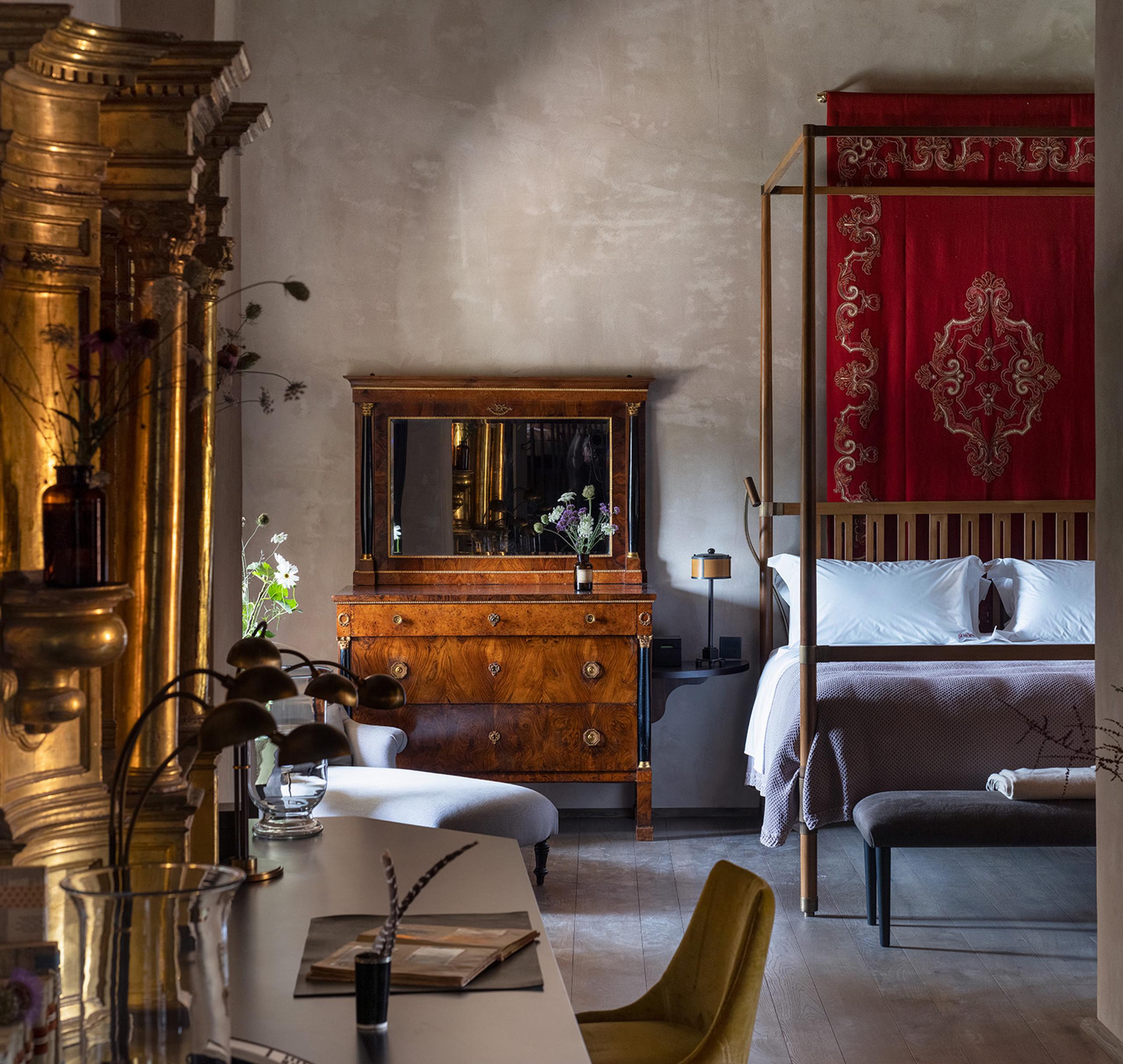 Castello di Reschio: a suite bedroom with a red canopy bed, antique gilt furniture, and a mustard chair on stone floors
