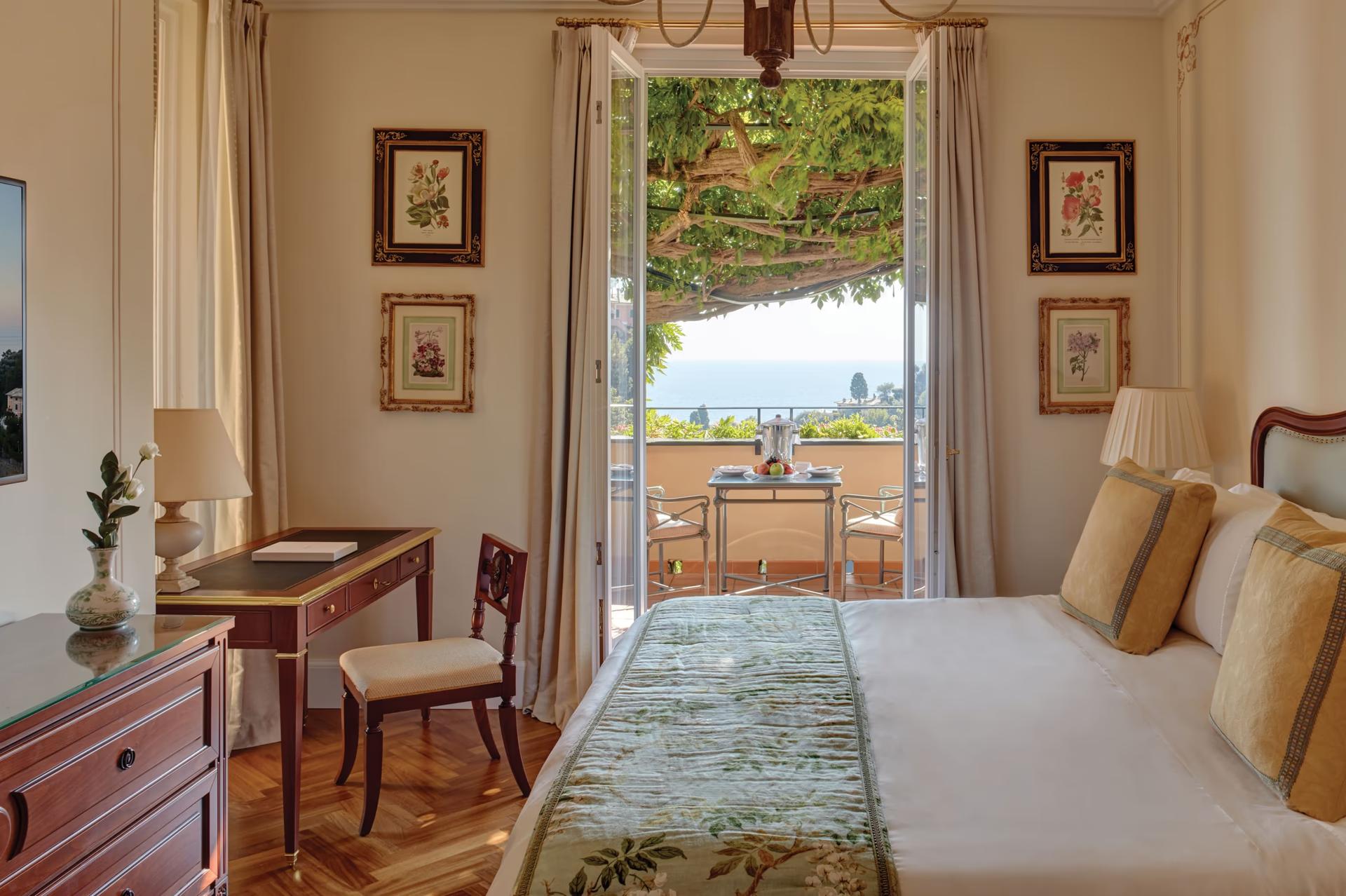 A bedroom with open doors to a sea-view terrace and classical Italian furnishings