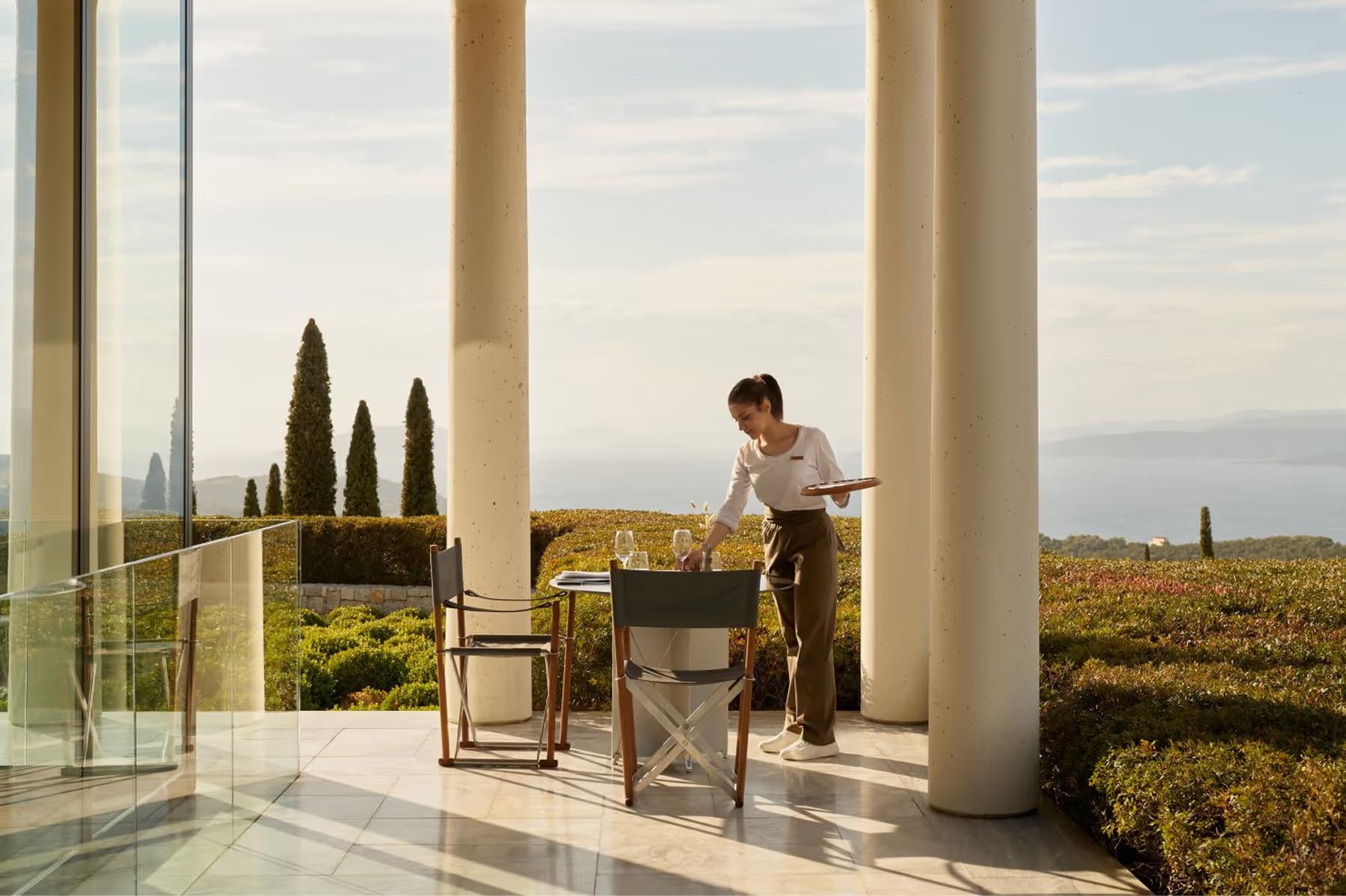 Amanzoe: server pouring wine at a columned restaurant overlooking the sea