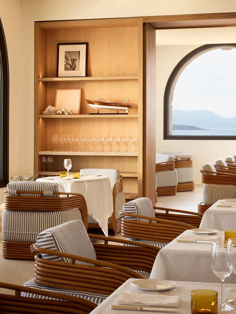 Rattan chairs with blue and white striped cushions at Delos Table, an arched window over the sea and hills