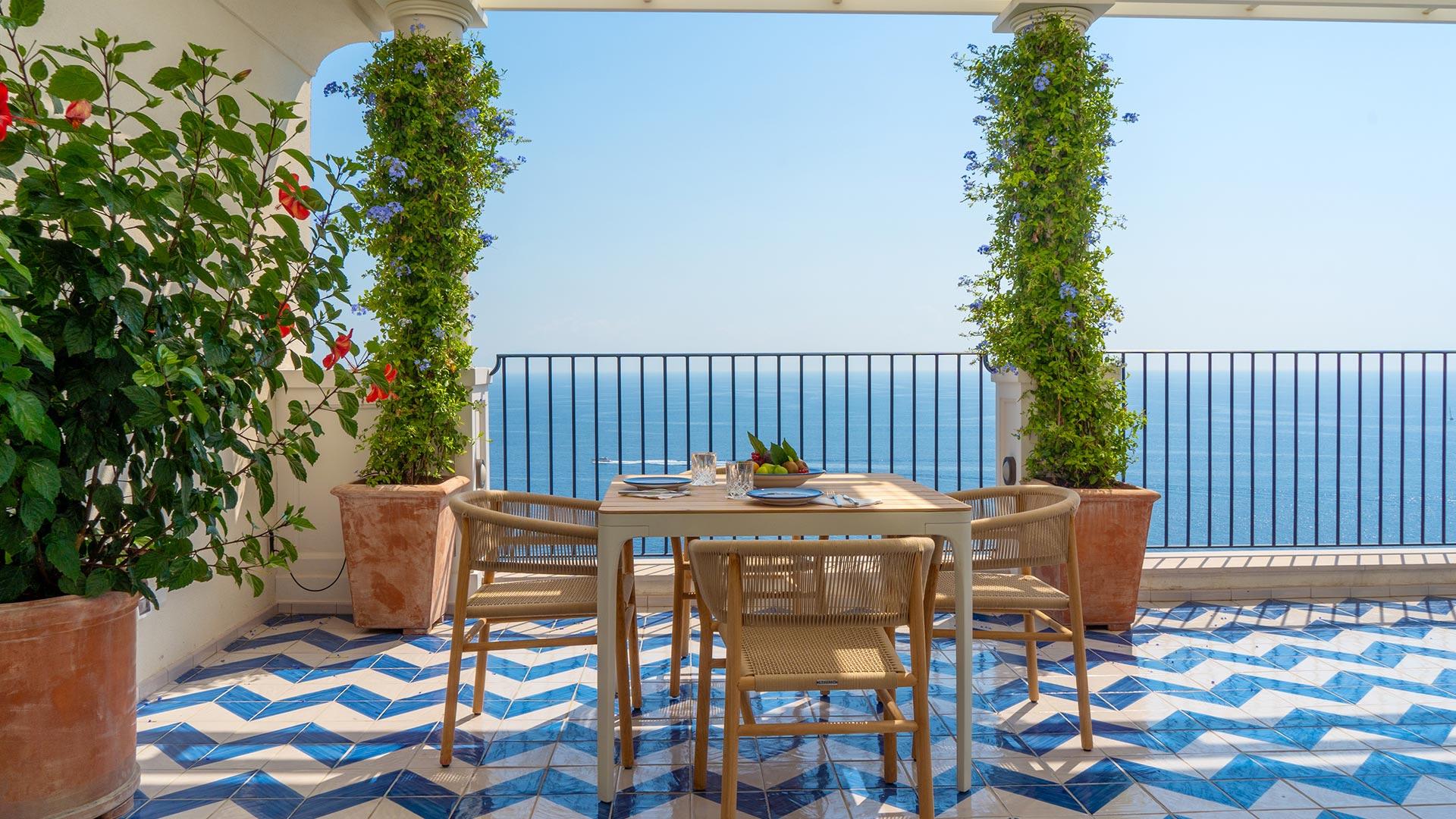 Borgo Santandrea: outdoor terrace table with wooden chairs overlooking sea, ivy-draped pergola frame