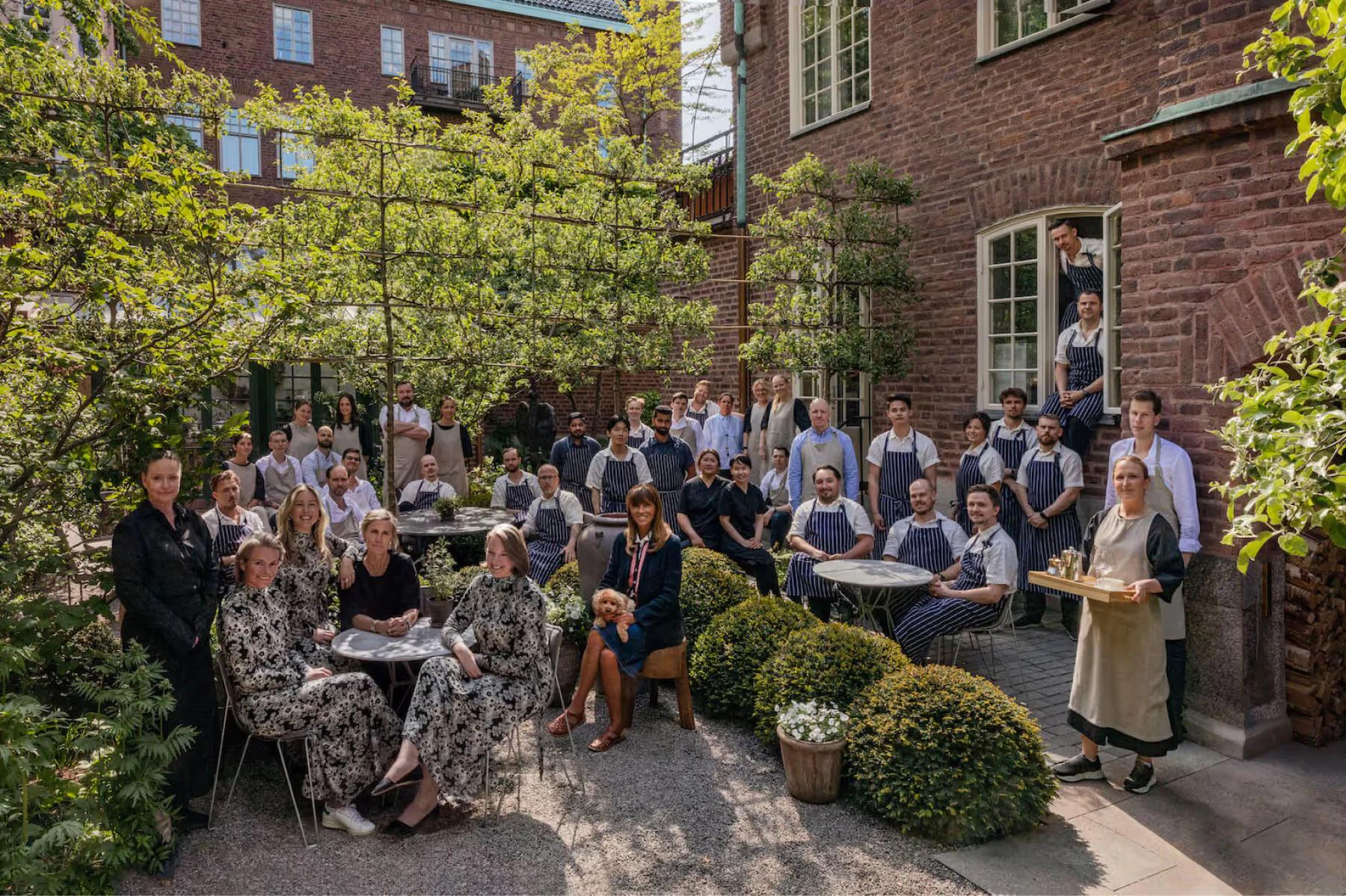 Ett Hem: guests gathered in a brick courtyard garden with trees and period architecture