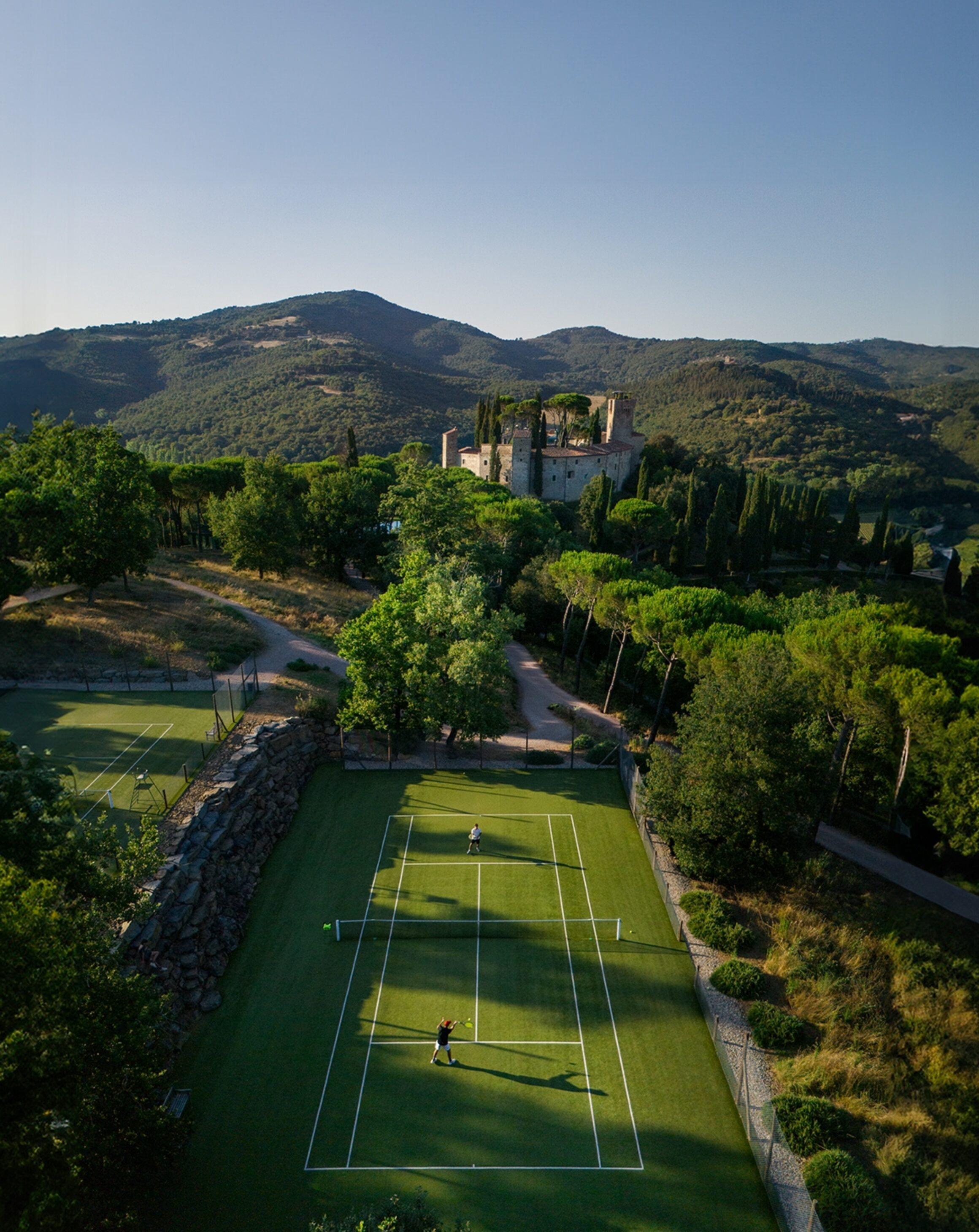An aerial view of the tennis court cut into the hillside, with the castle and wooded valley beyond