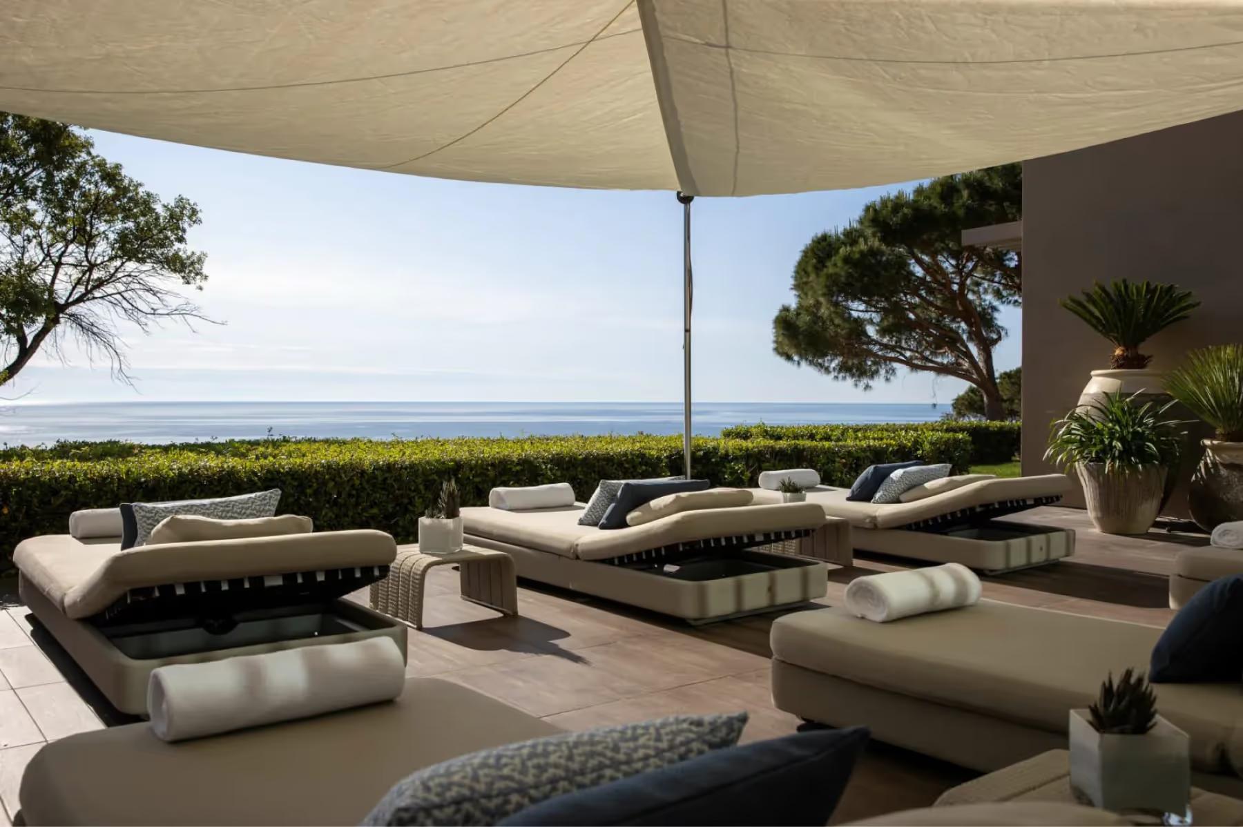 Shaded terrace with layered lounges and sea views beneath umbrellas