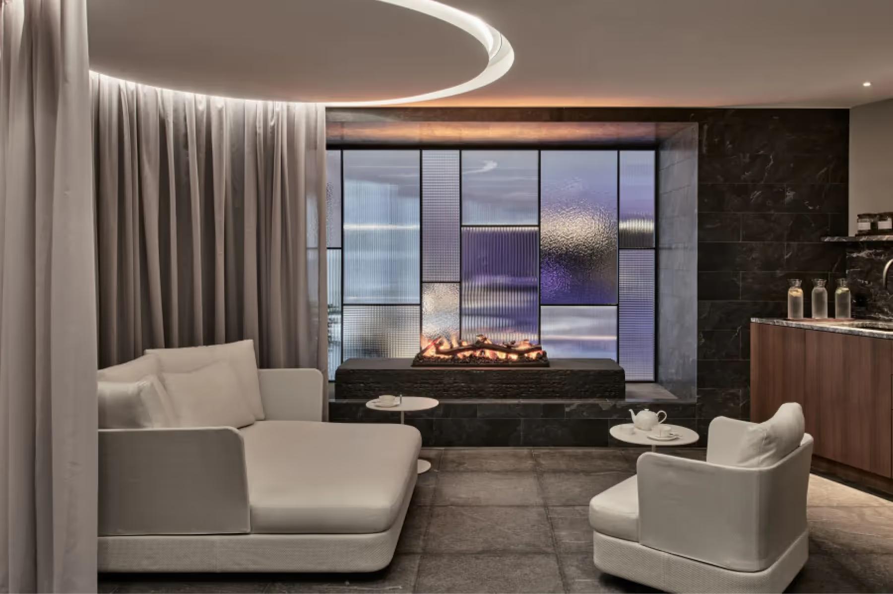 Grace La Margna St. Moritz: spa lounge with curved seating, fireplace, and windows overlooking evening mountain scenery