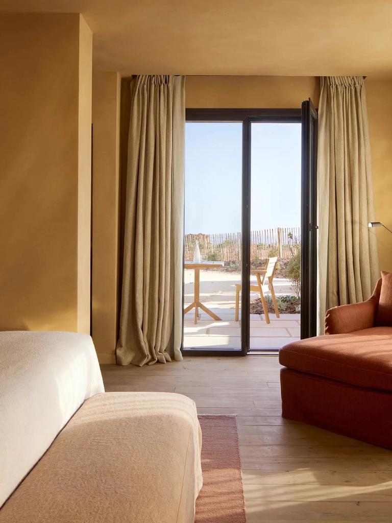 A Soukana room in ochre tones, glass doors open to a terrace with a wooden table and chair