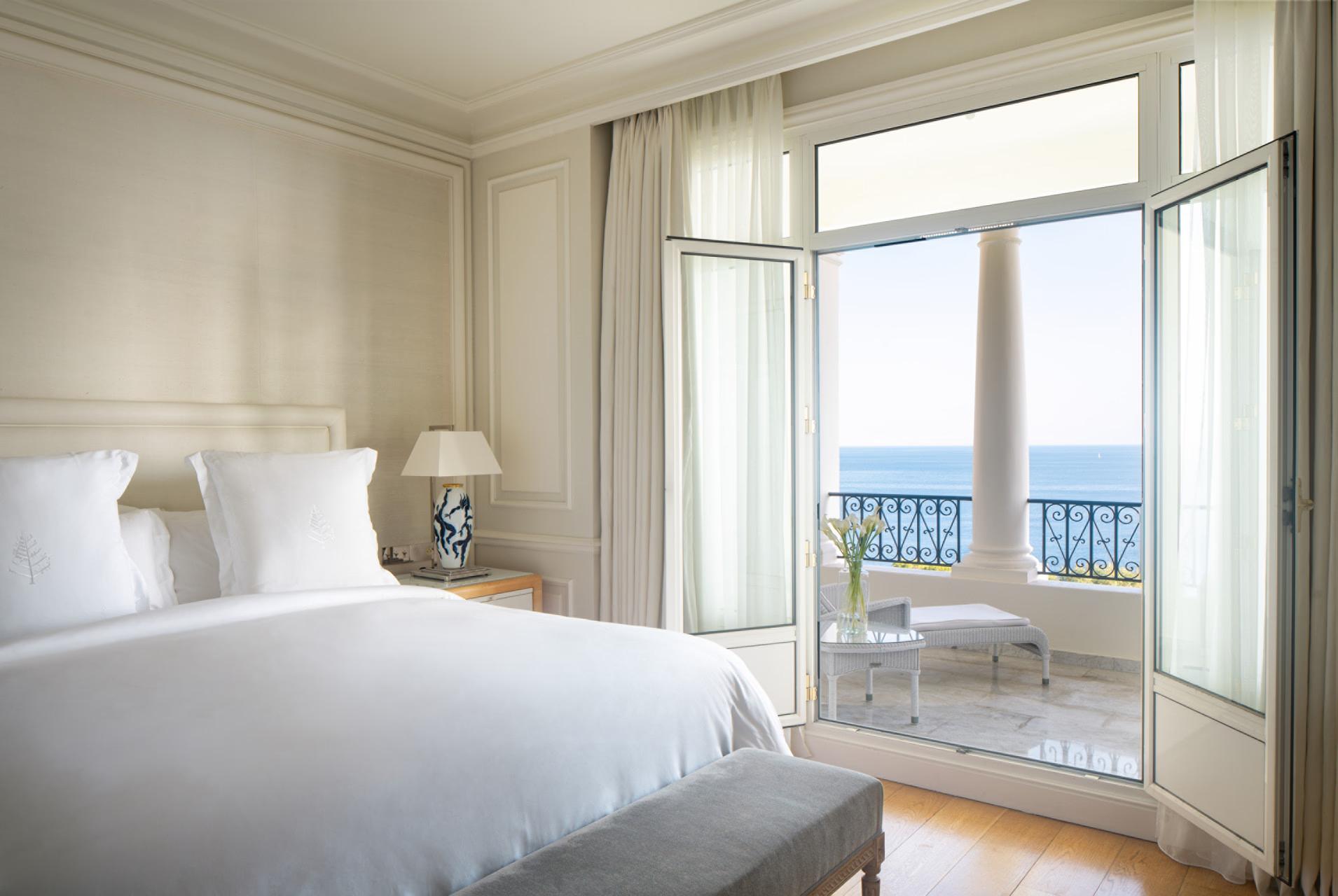 Bright bedroom with white linens and open doors to a sea-view balcony
