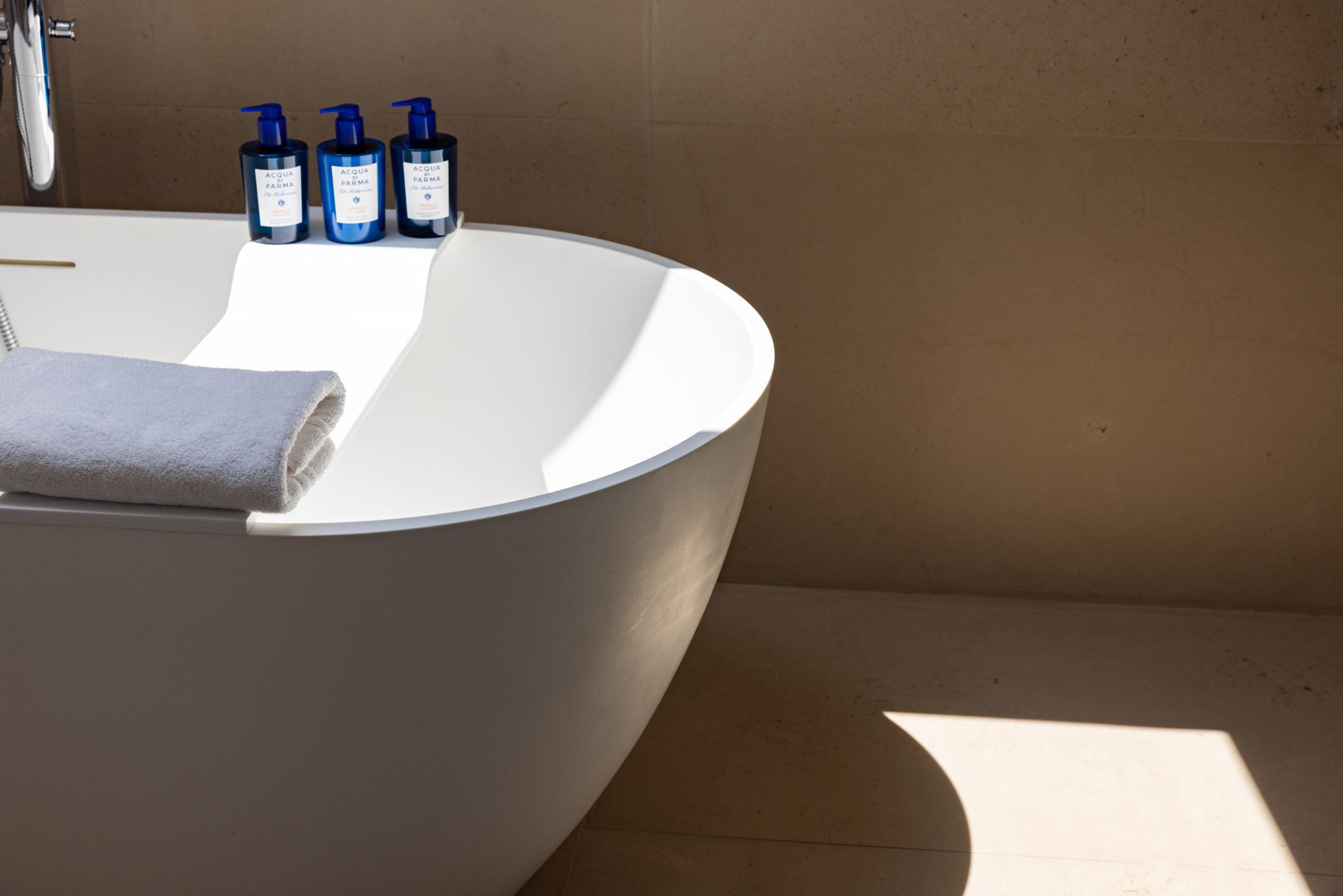A white freestanding bathtub with blue accent bottles, minimalist bathroom in warm tones