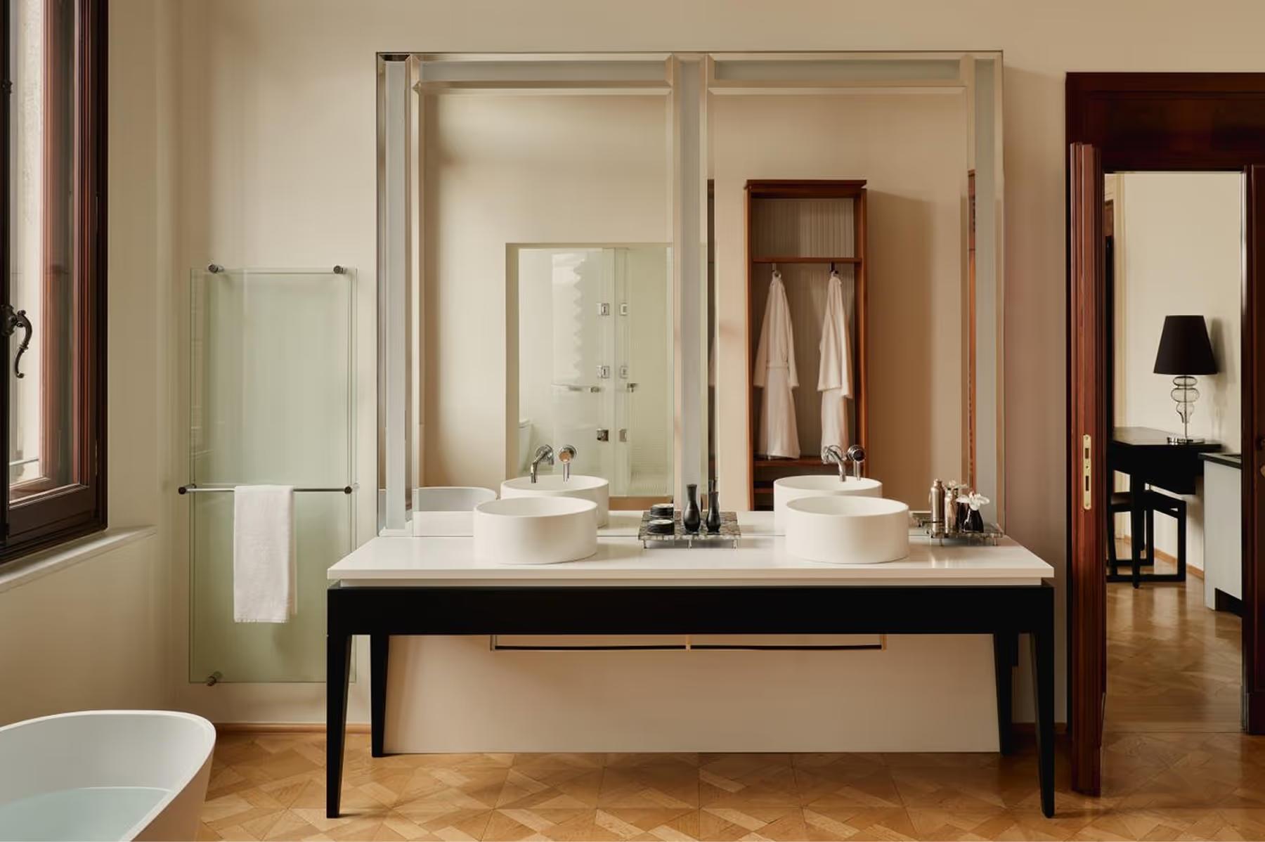 Aman Venice: a spa bathroom with double marble vanity, large mirror, glass enclosure, and wooden flooring